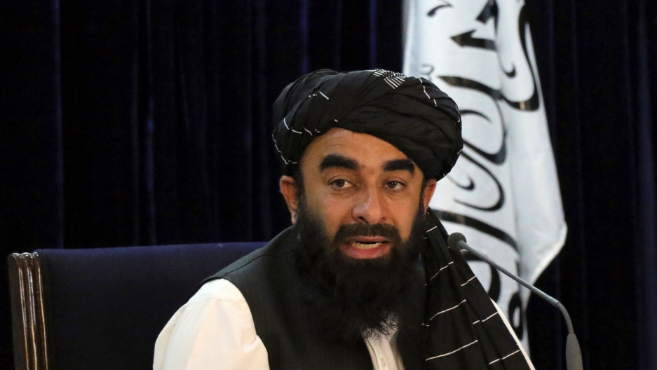 Taliban spokesman Zabihullah Mujahid speaks during a press conference in Kabul, Afghanistan, Sept. 7, 2021. The Taliban on Tuesday announced a caretaker Cabinet stacked with veterans of their harsh rule in the late 1990s. Taliban spokesman Zabihullah Mujahid is shown sitting while wearing a dark head wrap and black vest with the Taliban flag behind him.