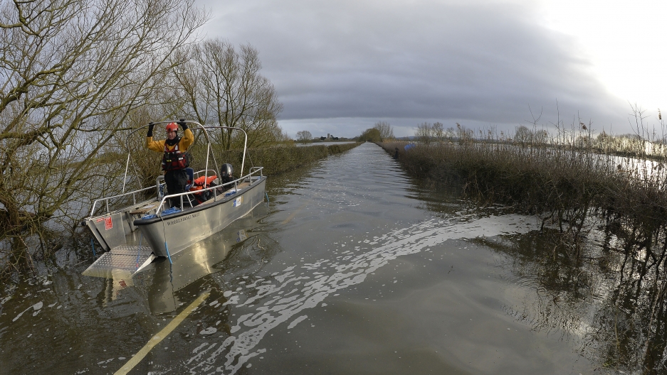 A boat operated by emergency services personnel waits to be driven down a flooded road to the village of Muchelney, seen in the background on the flooded Somerset Levels, near Langport in south west England January 27, 2014. Surrounded by flood water, Muc A boat operated by emergency services personnel waits to be driven down a flooded road to the village of Muchelney, seen in the background on the flooded Somerset Levels, near Langport in south west England January 27, 2014. Surrounded by flood water, Muc