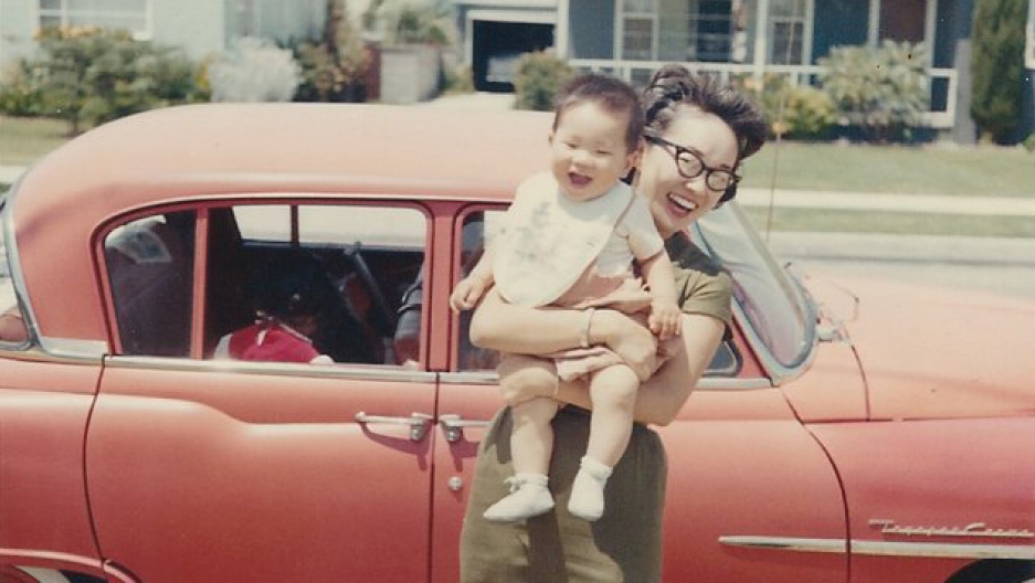 Bruce Kaji's wife holding their son, Troy, in front of the family car, the Red Toyota Toyopet, circa 1961. Bruce bought the car in 1958 from Hollywood Toyota. Bruce Kaji's wife holding their son, Troy, in front of the family car, the Red Toyota Toyopet, circa 1961. Bruce bought the car in 1958 from Hollywood Toyota.