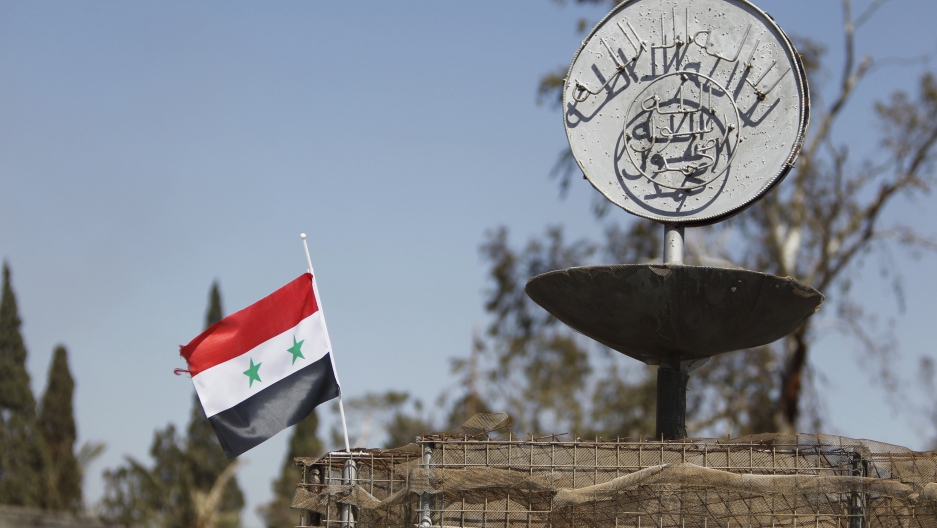 A Syrian national flag flutters next to the Islamic State's slogan at a roundabout where executions were carried out by ISIS militants in the city of Palmyra, in Homs Governorate, Syria April 1, 2016.