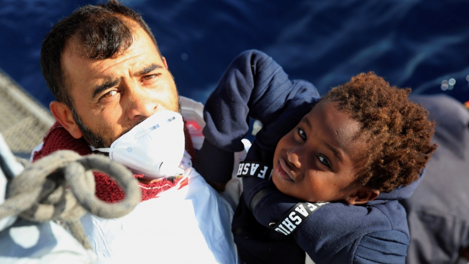 Man on a boat lifting a young child to hand to rescuers