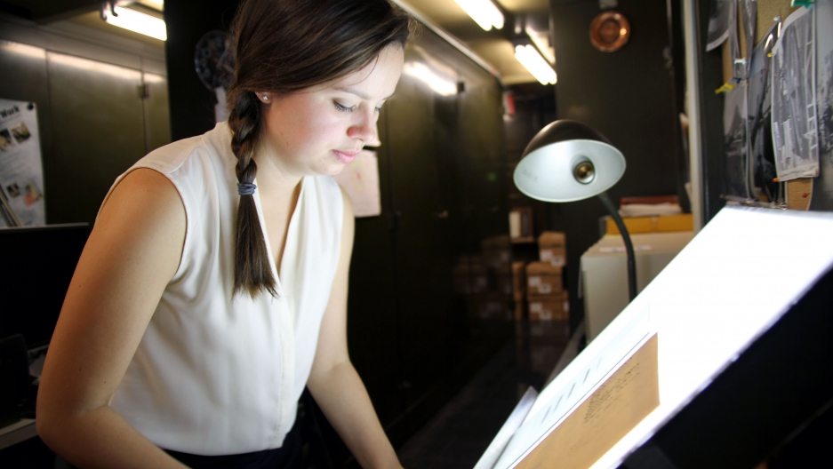 Lindsay Smith Zrull carefully places a glass plate photograph of the sky on a lightbox in the Plate Stacks room at the Harvard-Smithsonian Center for Astrophysics.