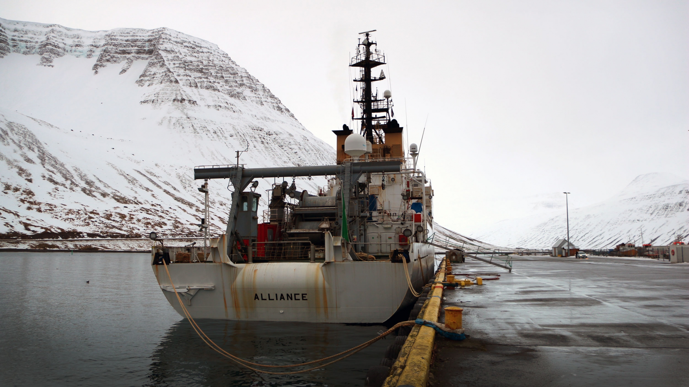 A boat is tied to a dock. Behind it are mountains covered in snow.