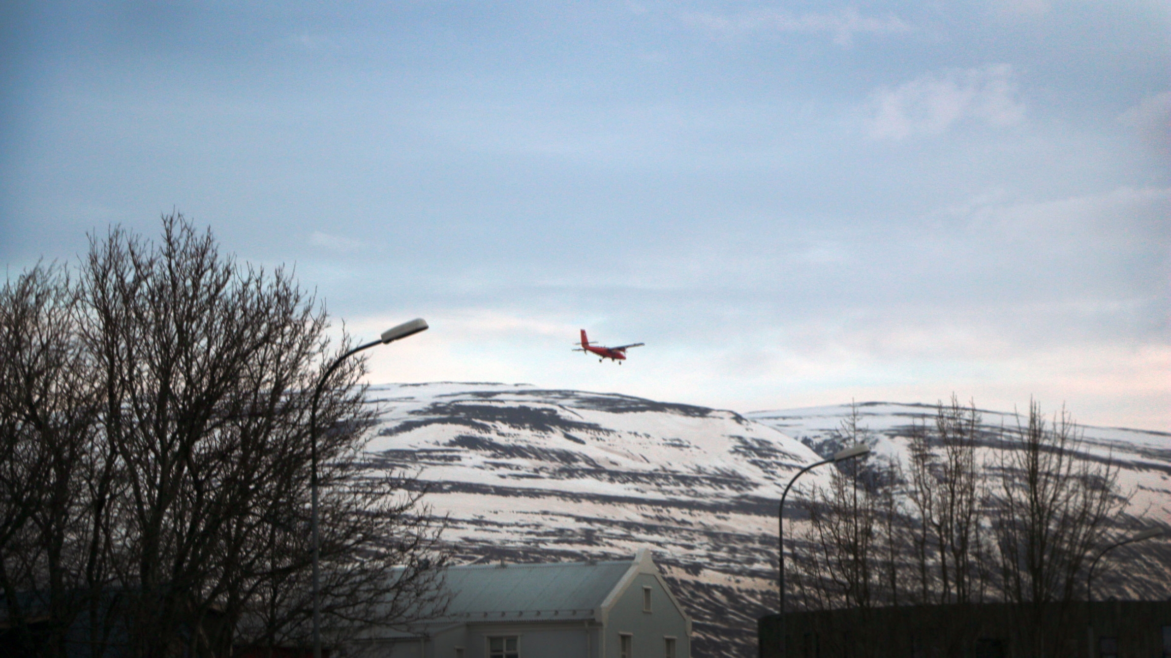 A red plane is seen in the sky above snow covered mountains and a small village