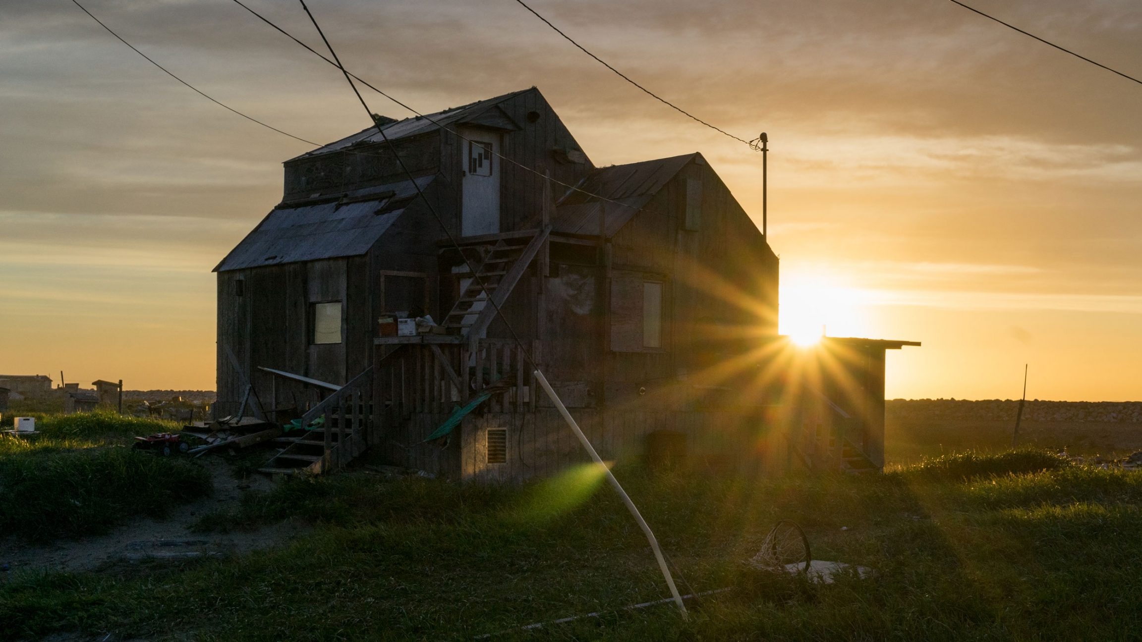 The sun sets behind a wooden home