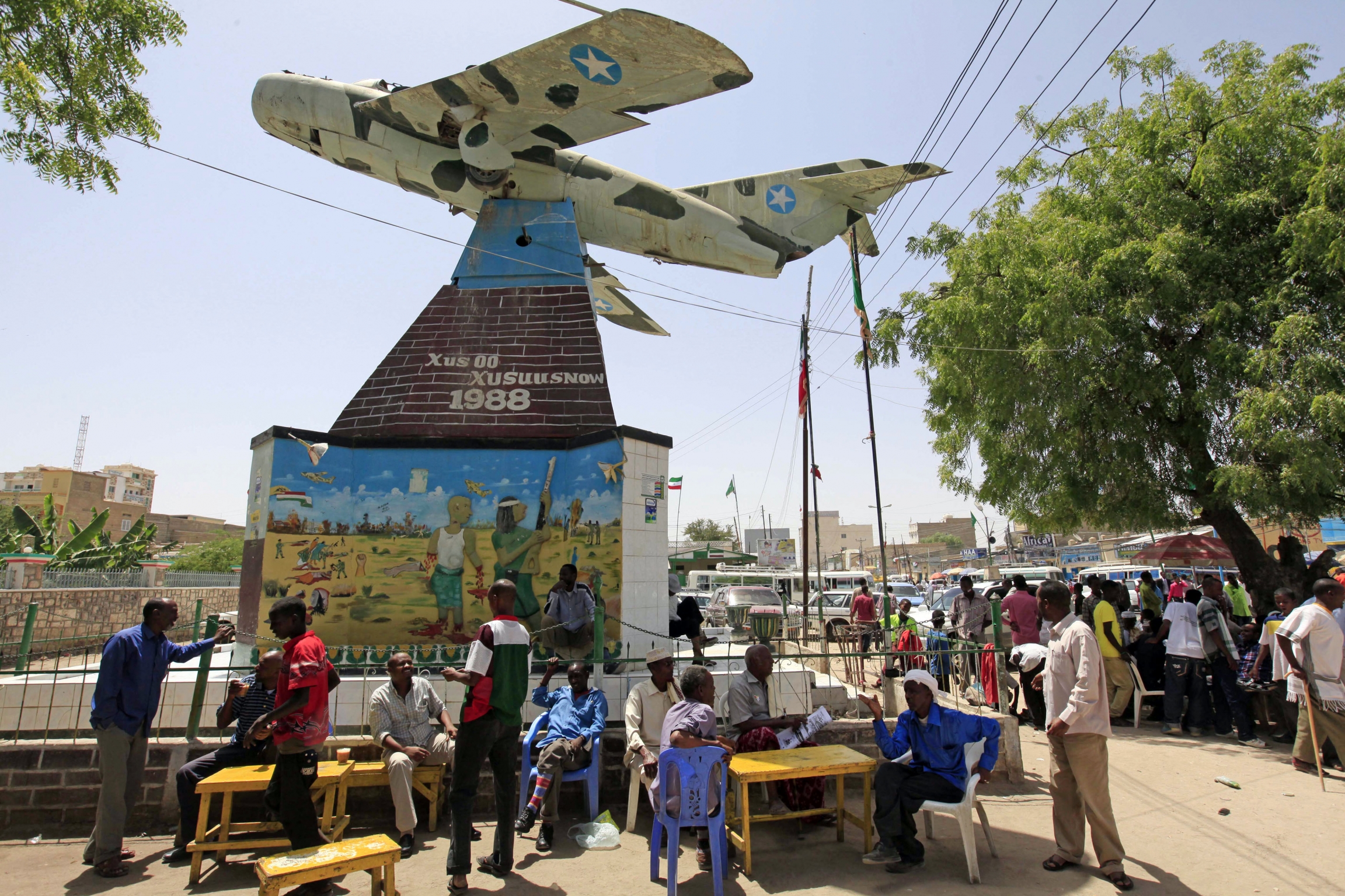 People stand underneath a war memorial in shape of airplane.