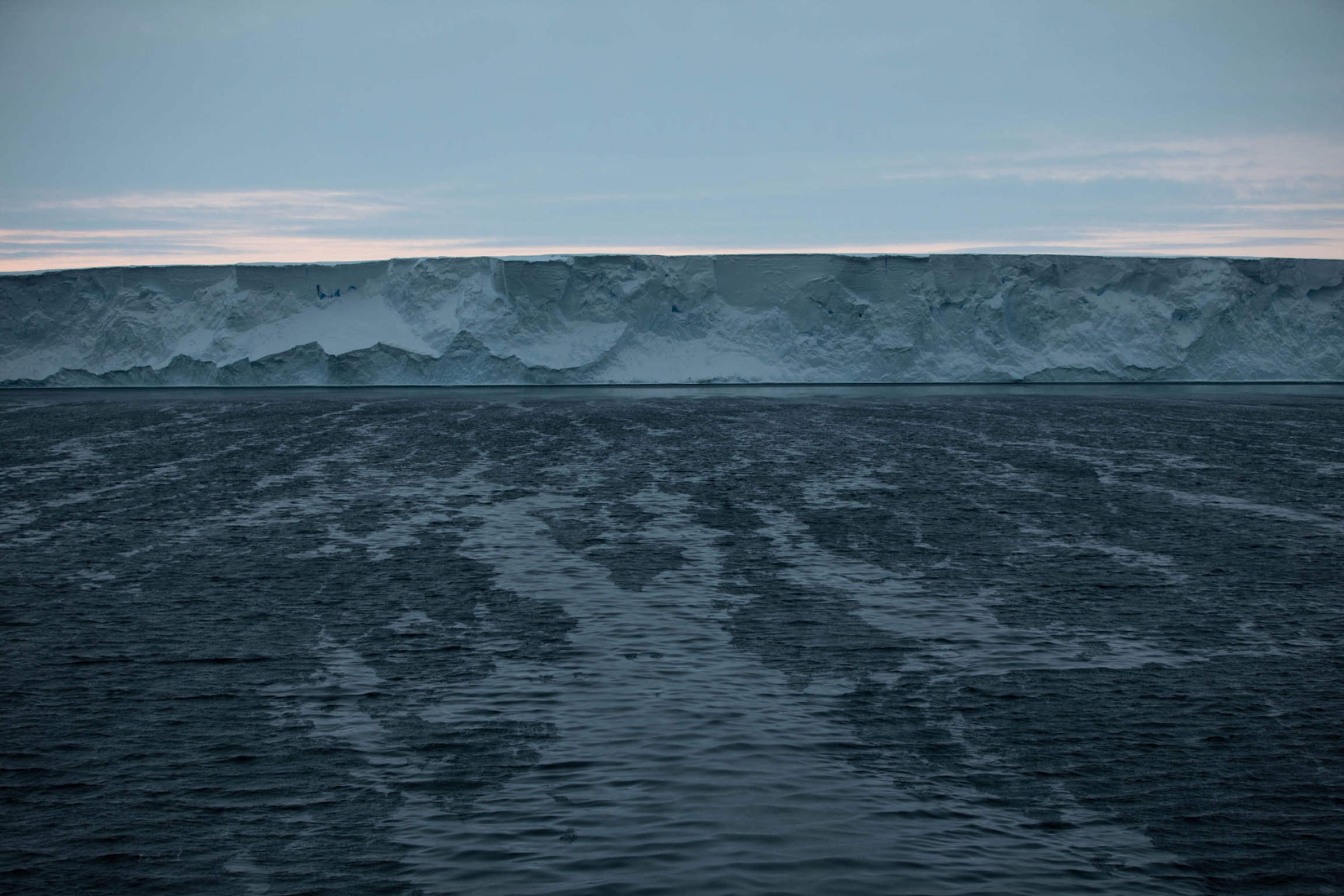 Grease ice forms before sunrise in front of Pine Island Glacier. Grease ice forms in front of a the large horizontal ice face of Pine Island Glacier.