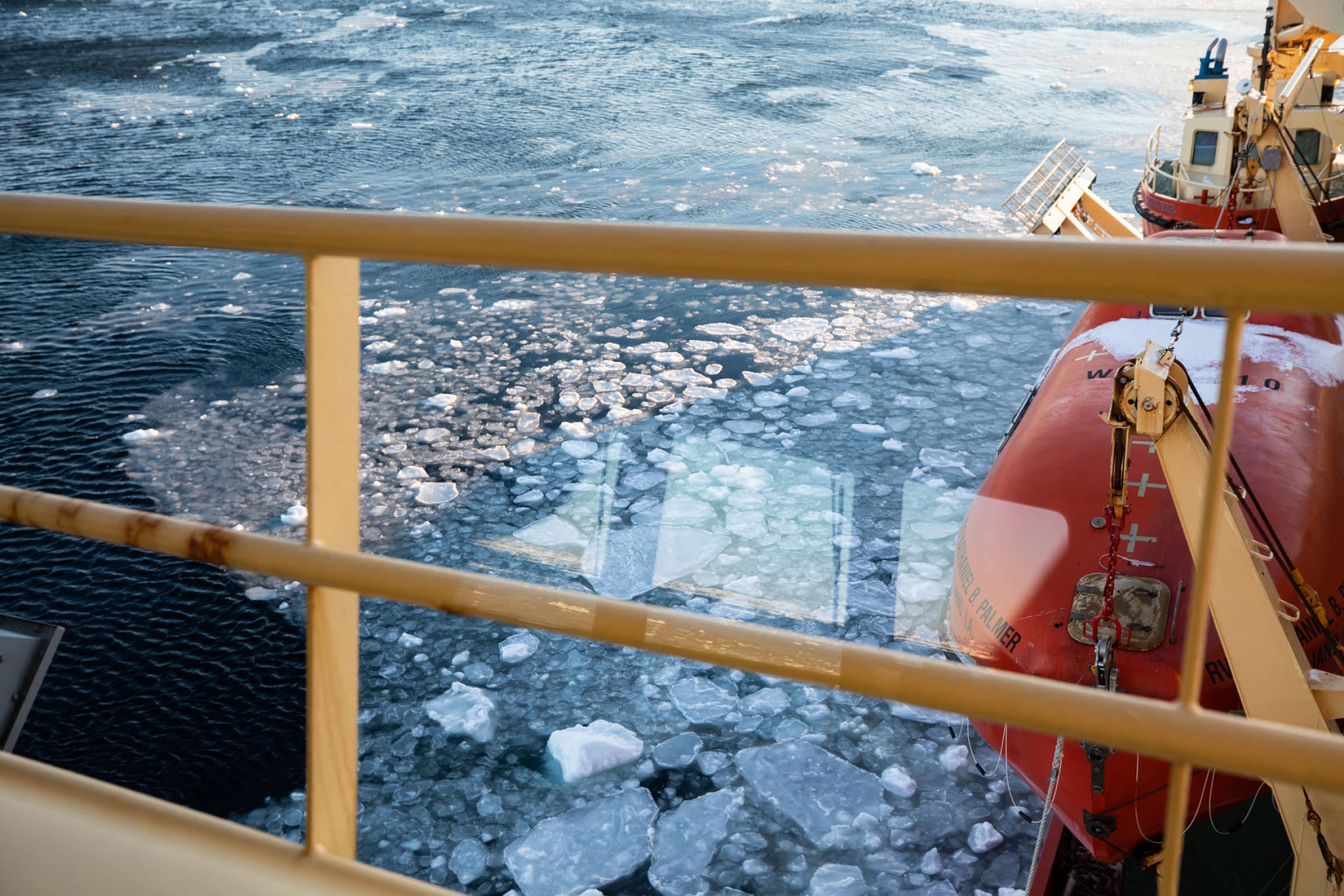 Larger pancake ice forms in the Amundsen Sea. The yellow railing of the a research vessel is in the nearground with ice shown forming in the Amundsen Sea.