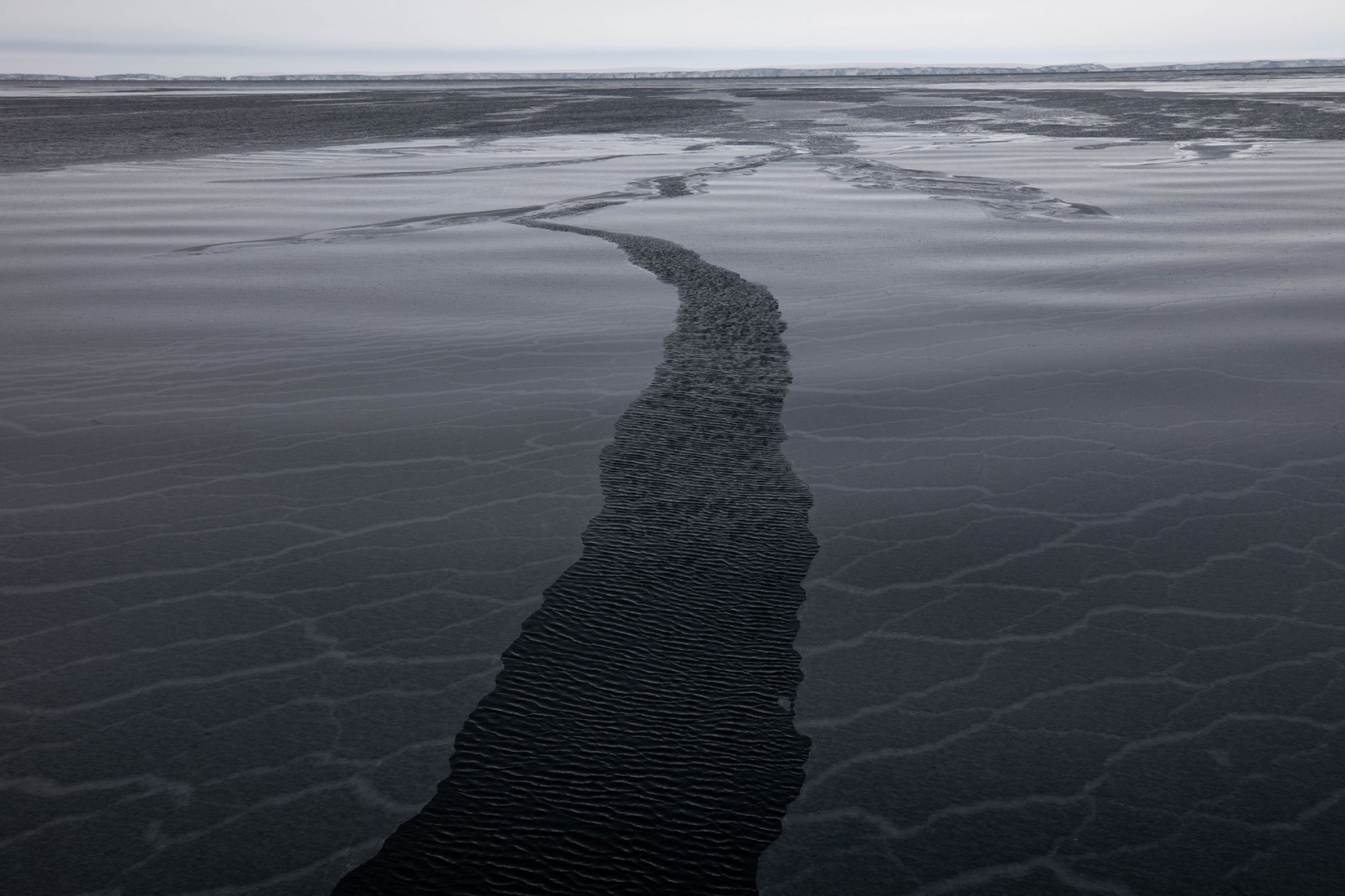 The wind cleaves a break in new ice on a gray day in the Amundsen Sea. A narrow break in new ice is shown in the middle of the photo on a gray day in the Amundsen Sea.