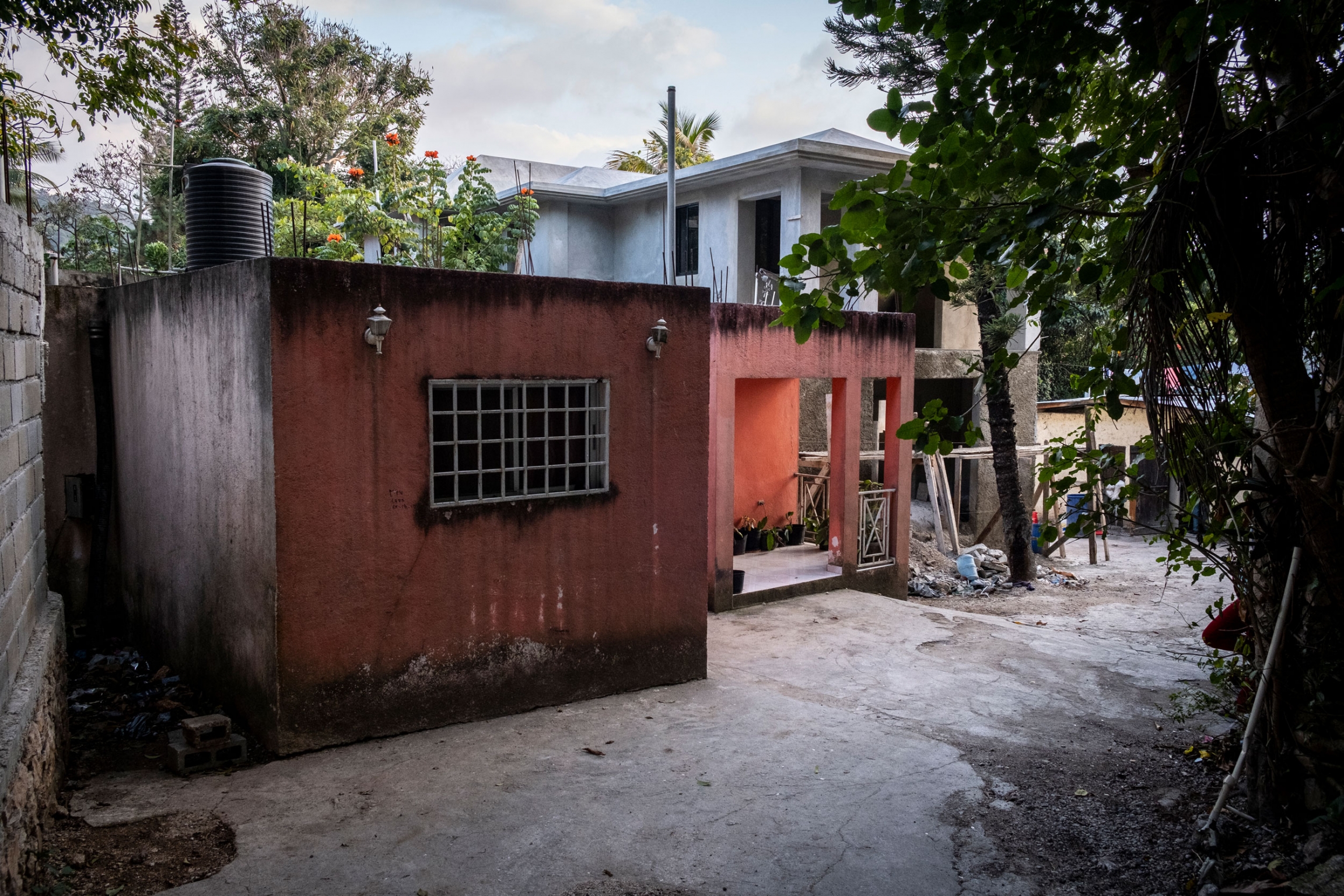 Before moving to Boston, Annette and her family used to live in this home. Now in the US and protected by TPS, she is able to send her family money. A single story, red building is shown with a metal grate covering a window.