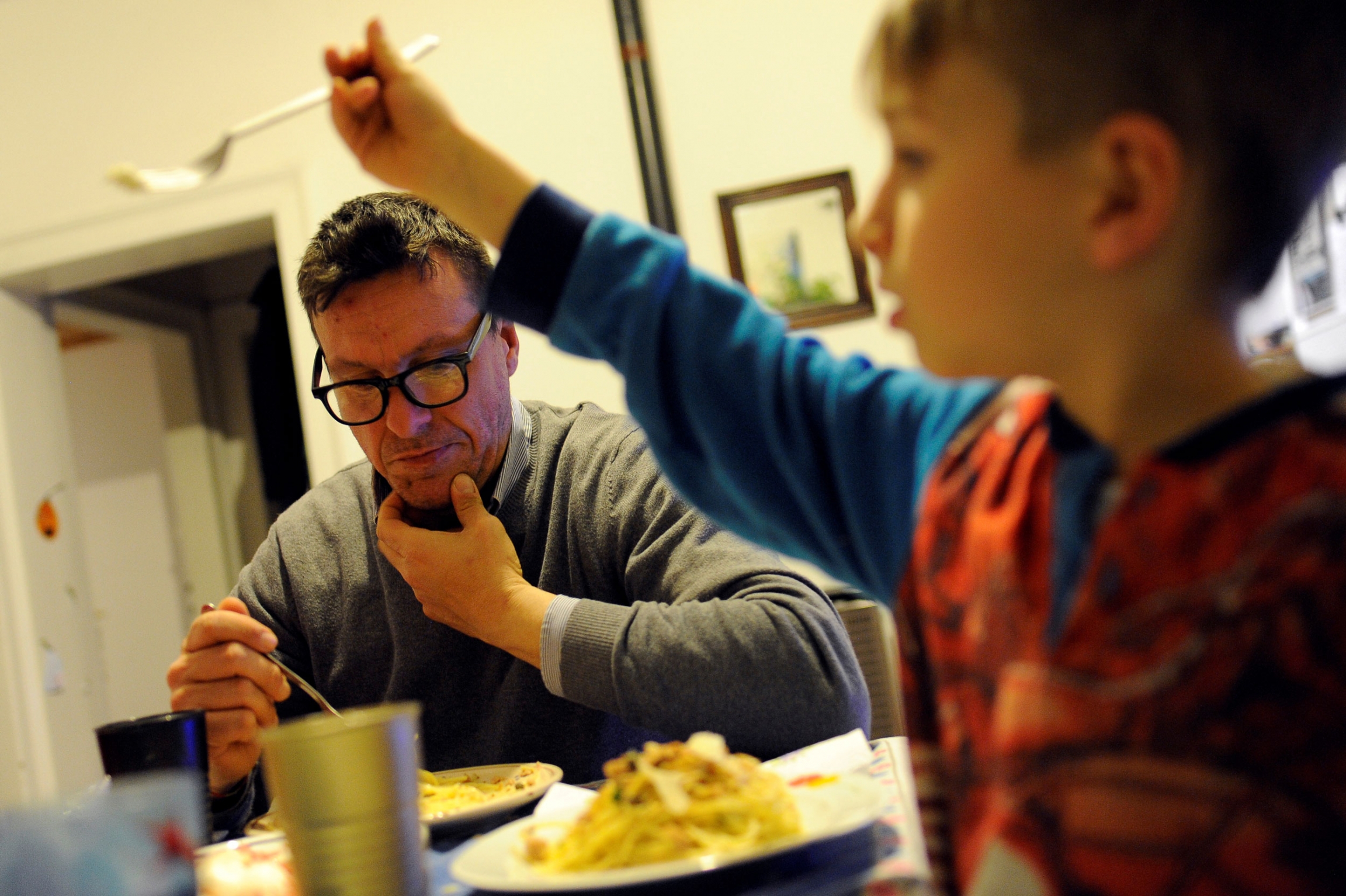 Spokesman of Social Assembly for the House (ASC) Nicola Ussardi, 41, eats dinner in his illegally occupied apartment in Venice, Italy. A young boy is shown in the nearground of the photo holding up a fork with his father sitting in the background eating from a plate of food.
