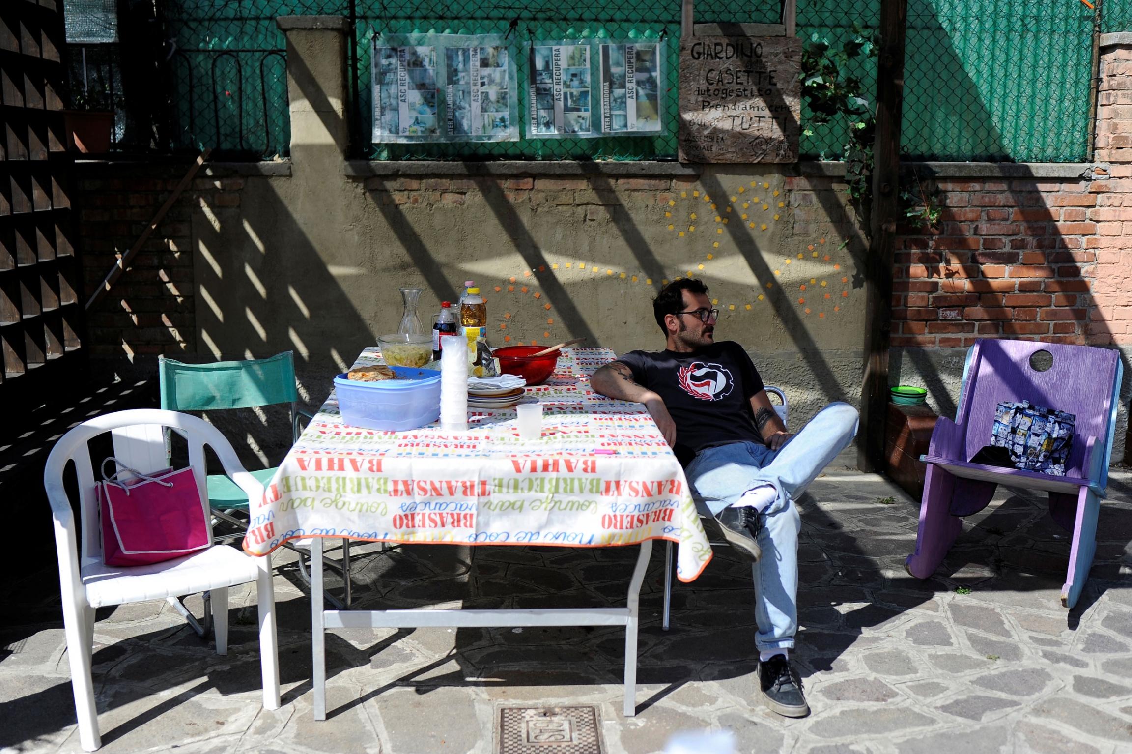 Pasquale Ambrogio sits outside his illegally occupied apartment during a lunch organized by squatters in Venice. A young man wearing a mustache, dark rimmed and a t-shirt and jeans is shown sitting at a table with food sitting out.