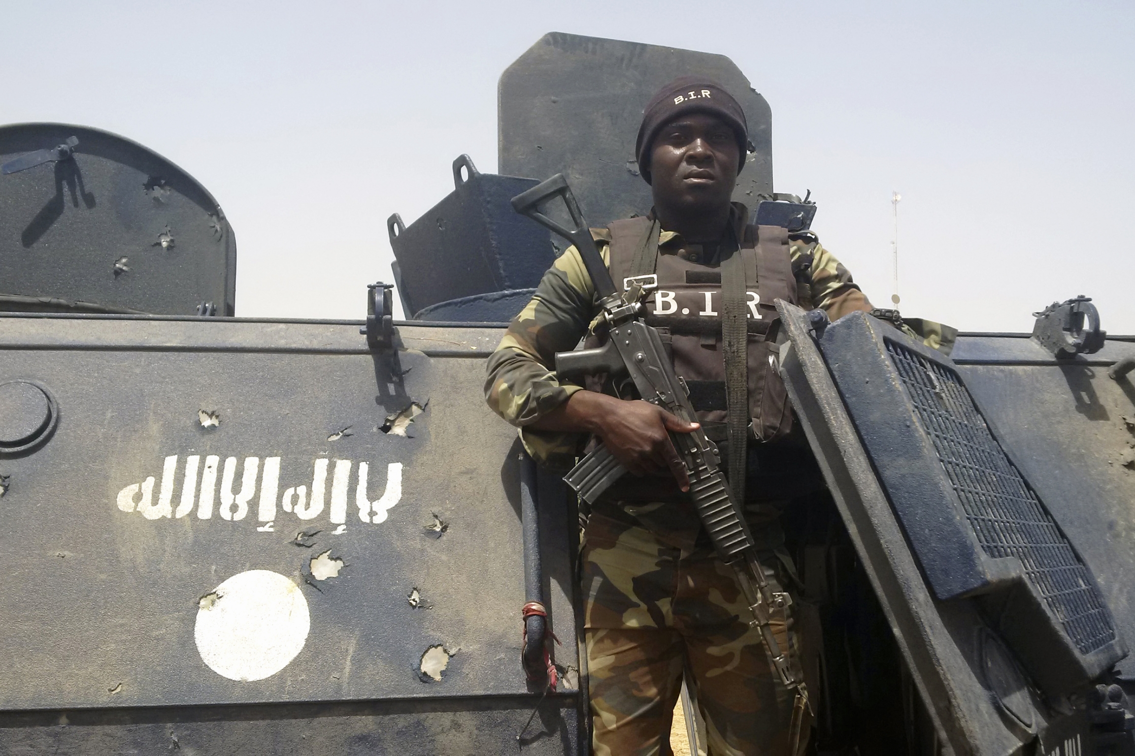 Cameroonian soldier stands near tank with Boko Haram logo on it.