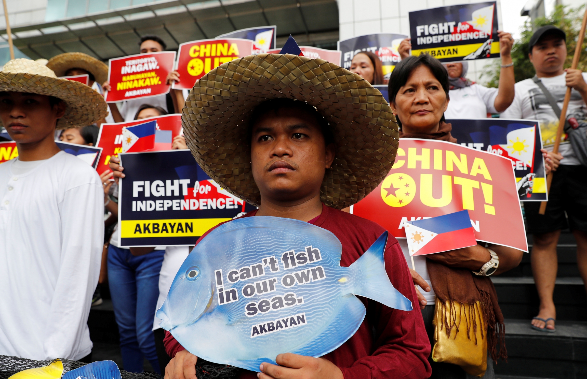 Man wearing straw fishing hat carries sign that says "I can't fish in my own waters."