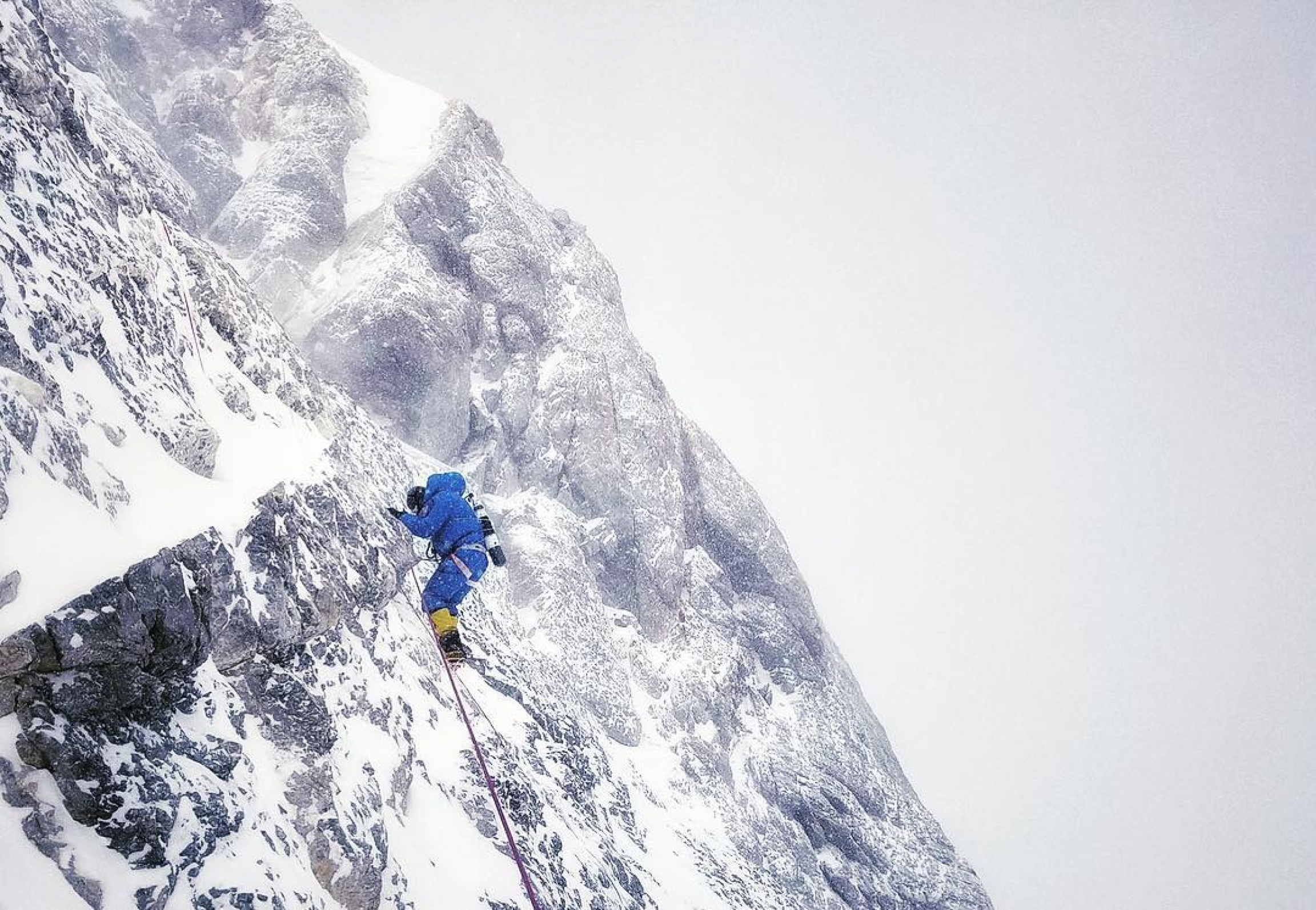 Richards climbing Everest 2016 A person wearing blue mountain climbing suit and yellow boots climbs a rocky face on Mount Everest