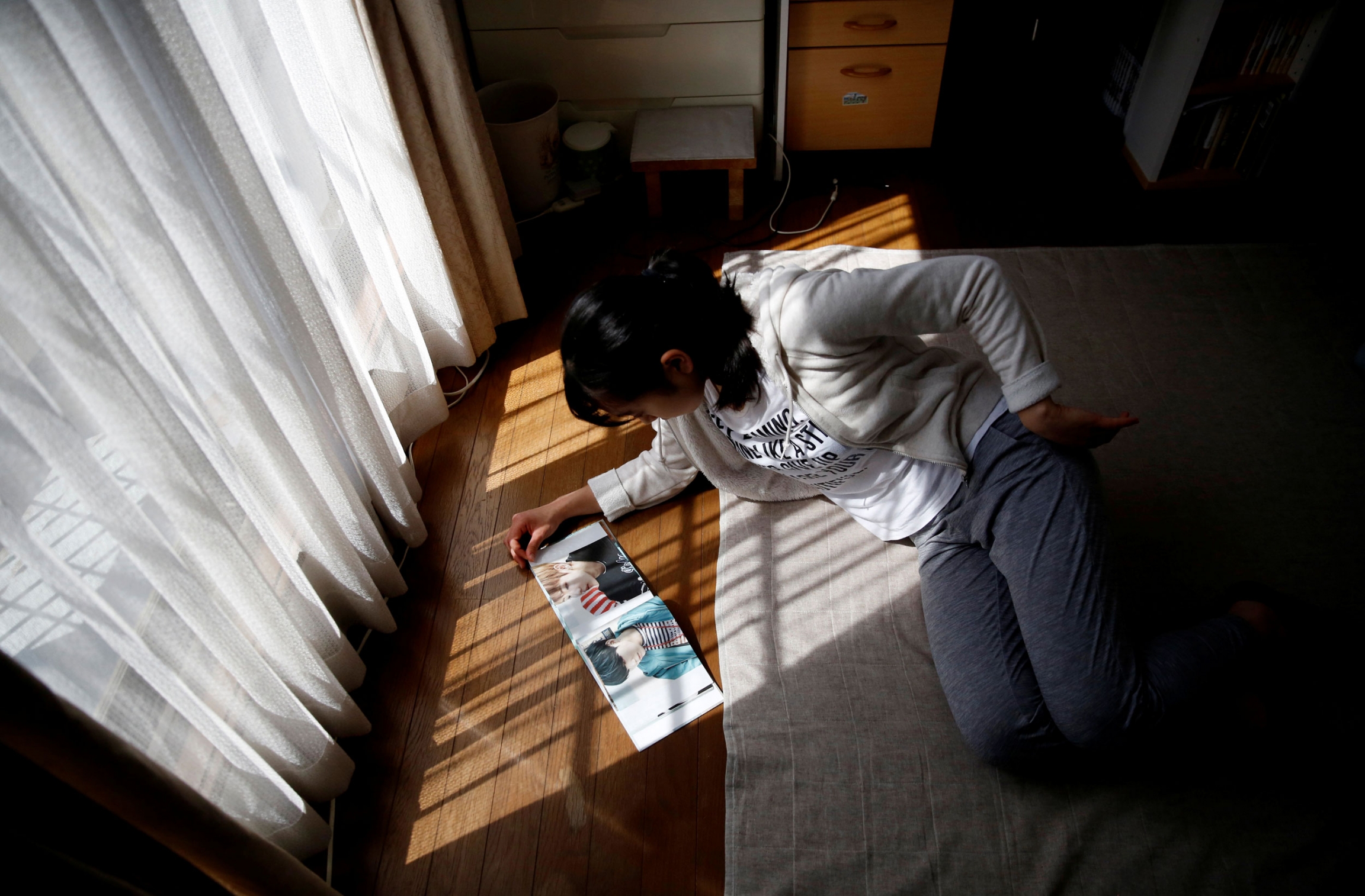 Niitsu looks at BTS's photo book in her room in Tokyo. A woman is shown laying on a carpet on the floor, clipping through a book with pictures.