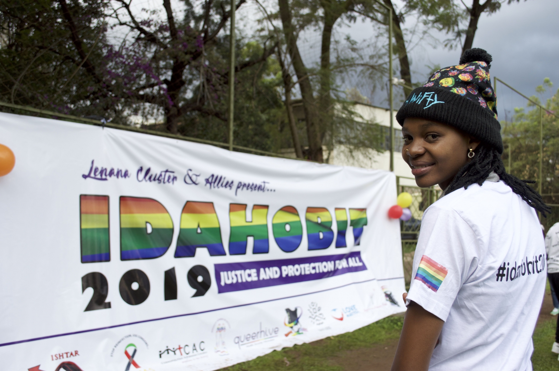 A queer person in Kenya stands near rainbow banner.