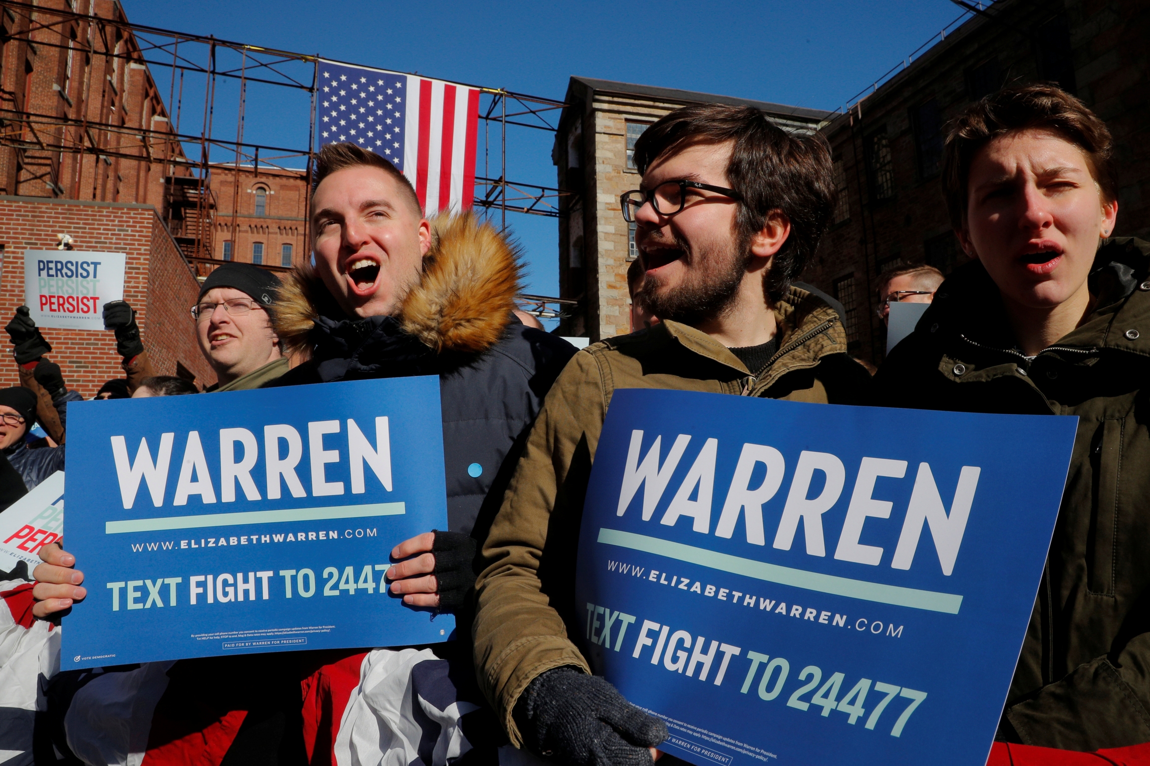 Supporters wait for U.S. Senator Elizabeth Warren at a rally to launch her campaign for the 2020 Democratic presidential nomination. Young men hold campaign signs for Elizabeth Warren.