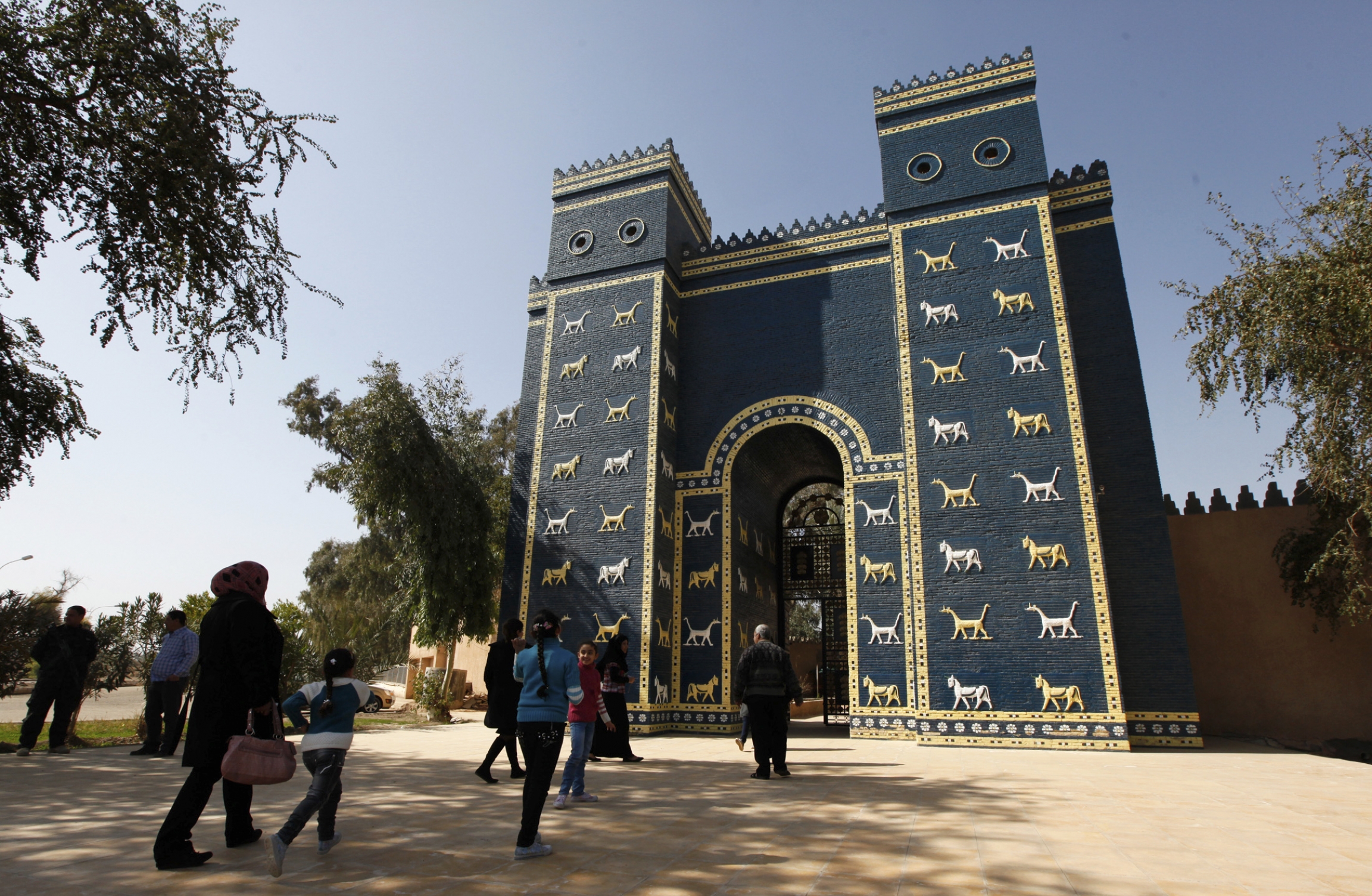 Residents visit a replica of the Ishtar Gate of Ancient Babylon near Hilla, south of Baghdad. People stand next to a blue gate.