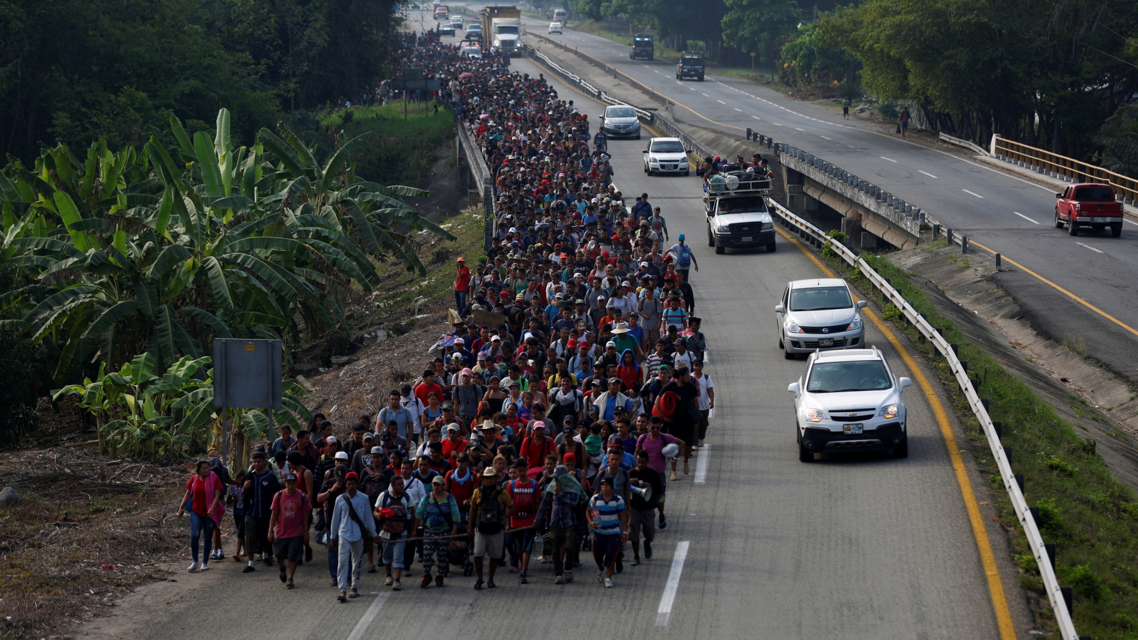 Central American migrants walk on a road in Villa Comaltitlan, Mexico, during their journey towards the United States in April 2019. A long line of people, hundreds and hundreds, walk in one lane of a highway in a large mass.