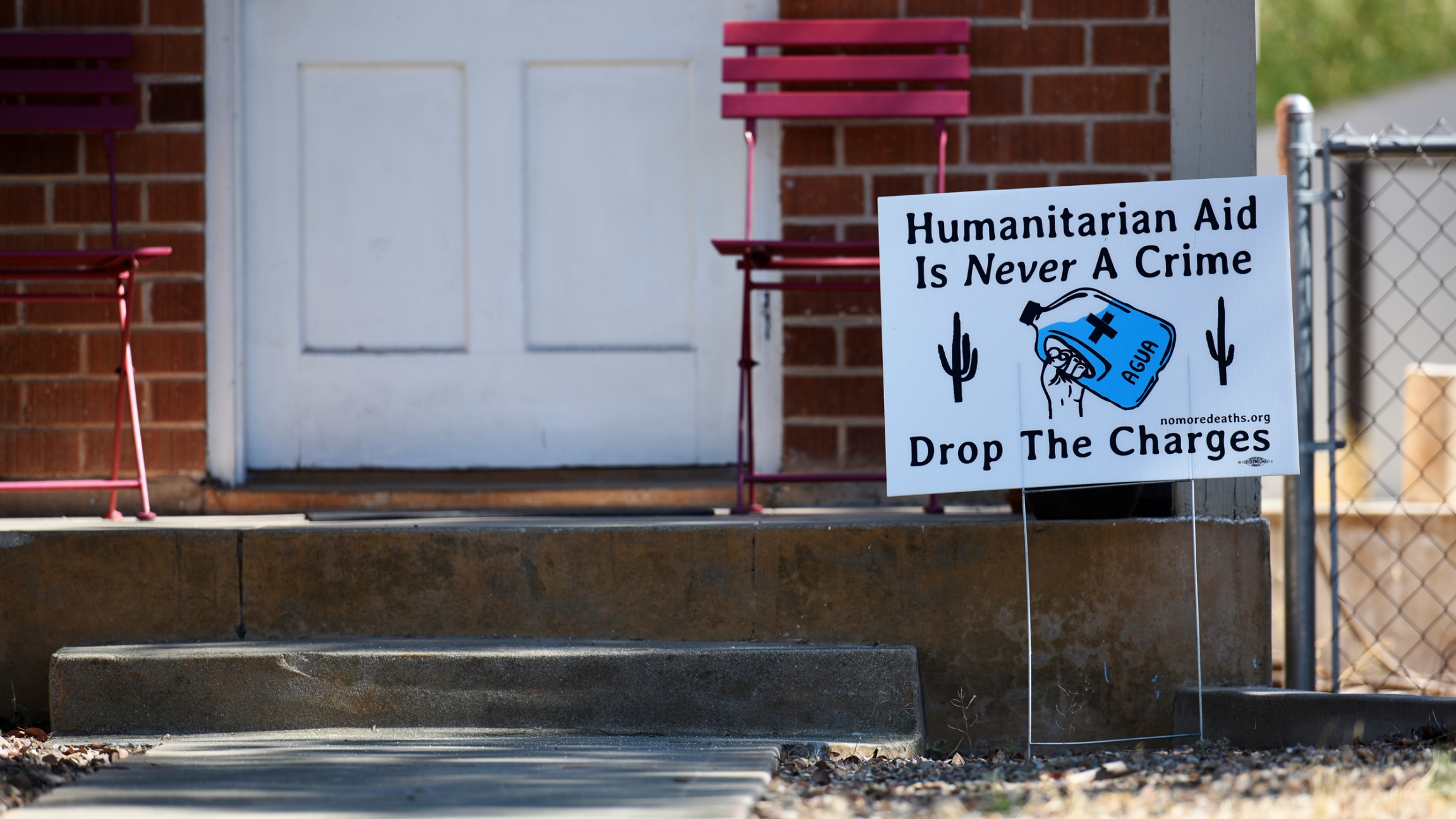 A yard sign in support of "No Más Muertes/No More Deaths" is displayed in the neighborhood surrounding the courthouse where humanitarian volunteer Scott Warren faces charges of harboring and conspiracy to transport undocumented migrants in Tucson, Arizona A yard sign says "Humanitarian aid is never a crime. Drop the charges." and includes a picture of a waterbottle and cactus.