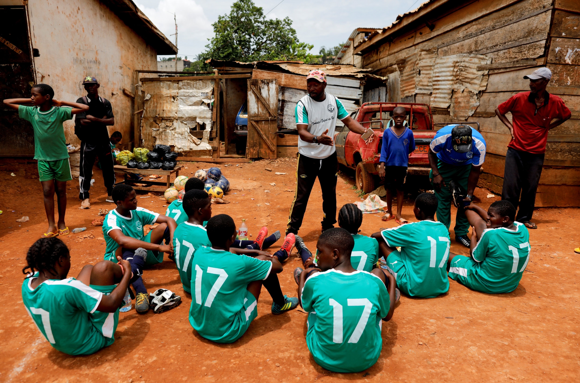 Biolo talks with his team during half-time. A coach is standing in front of his team whom are all sitting on the ground wearing green uniforms.