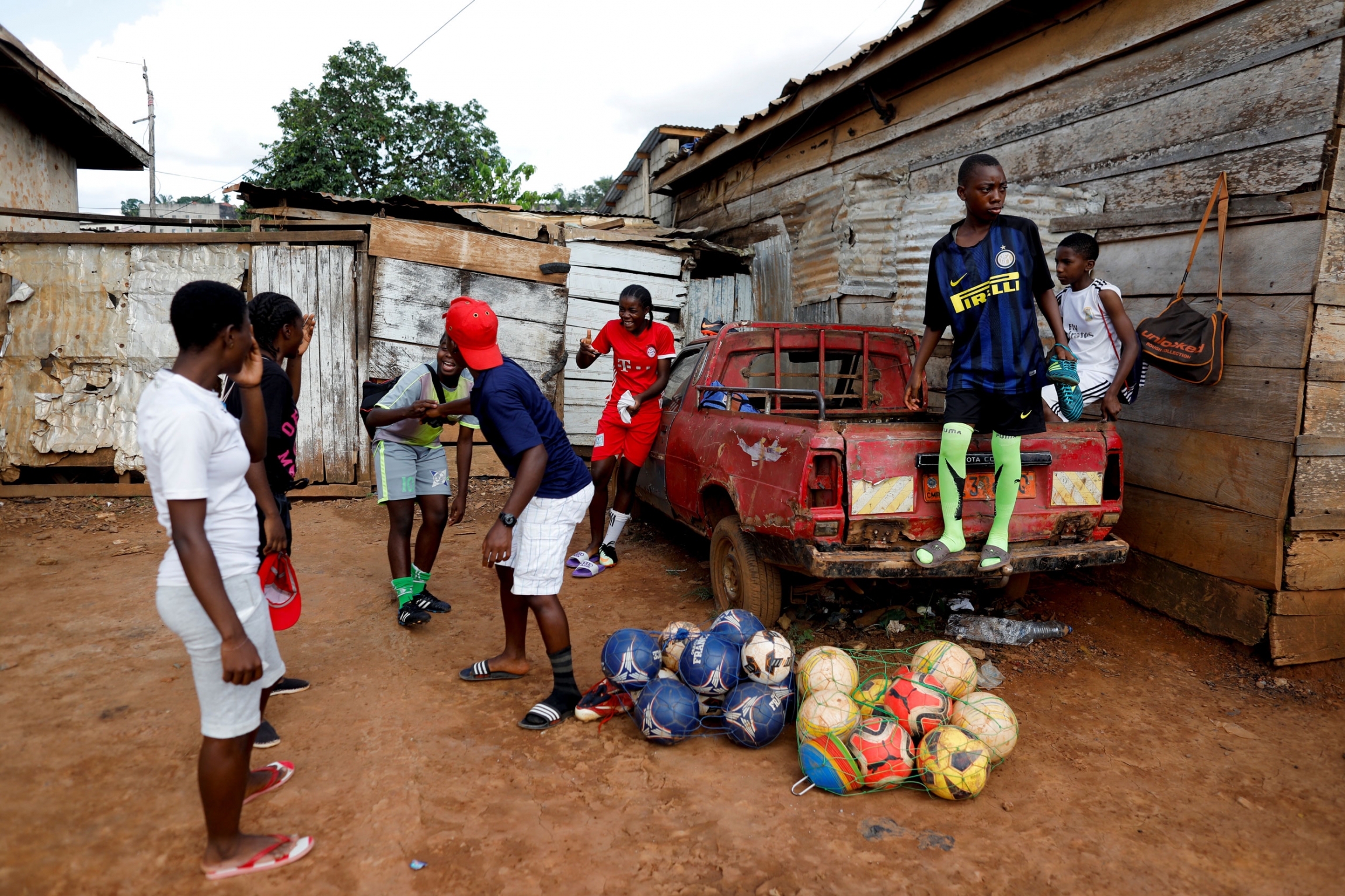 Asheri jokes with her teammates before their training session. A group of young people are shown standing around a red pickup truck laughing.