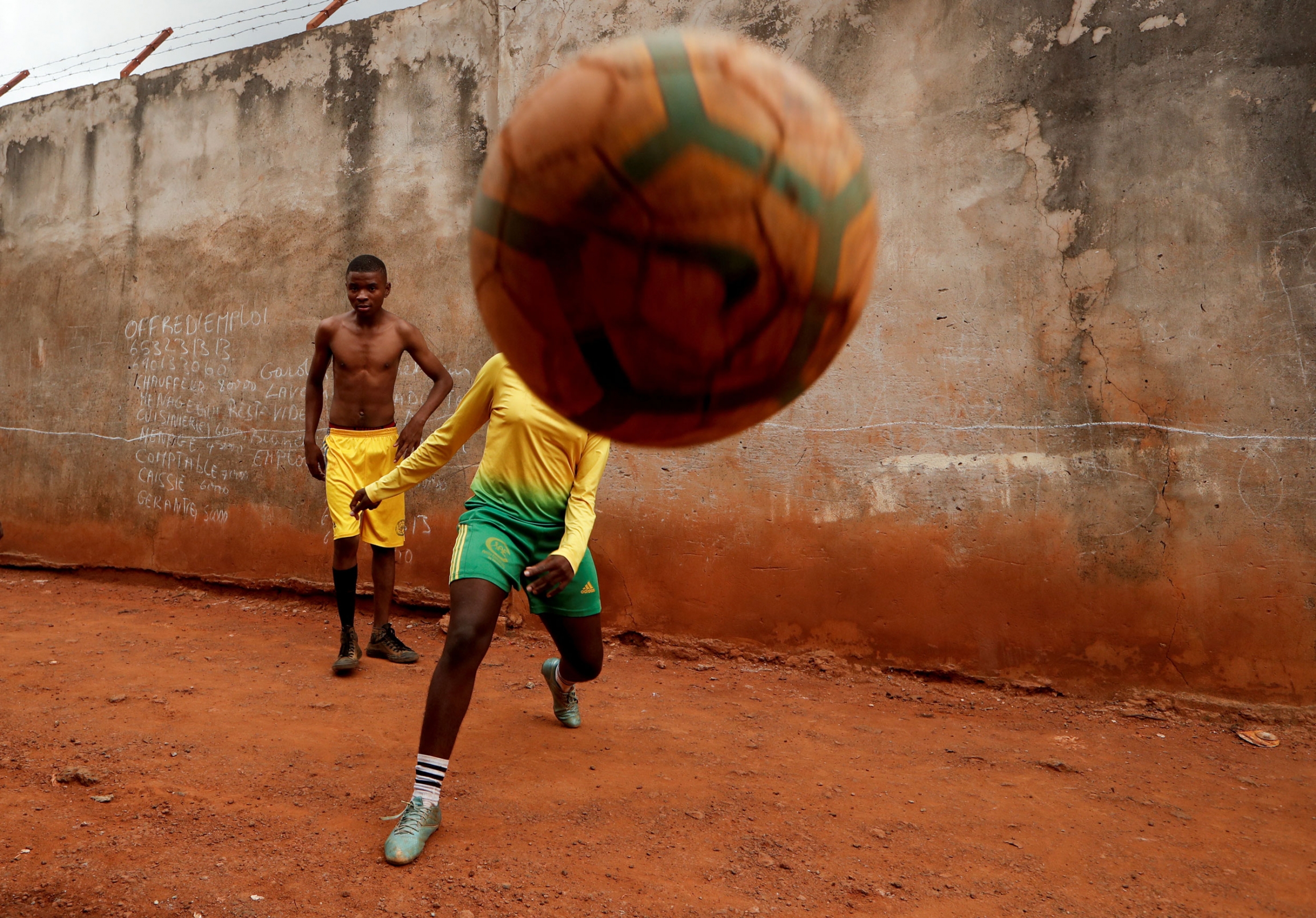 Asheri plays soccer with her friends outside her house. A young woman is shown kicking a soccer ball directly at the camera.