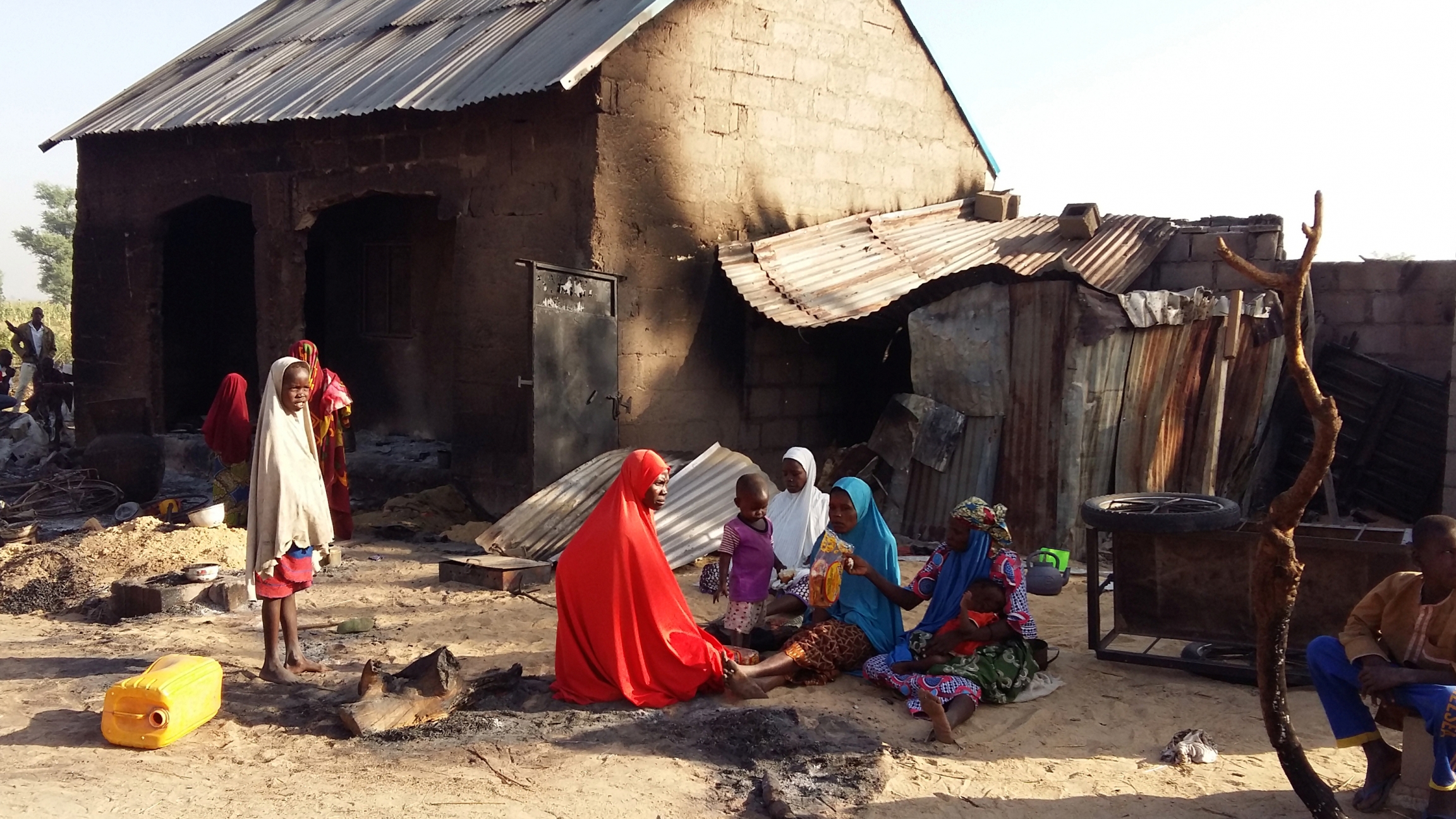 A family sits in front of a burnt house with their belongings.