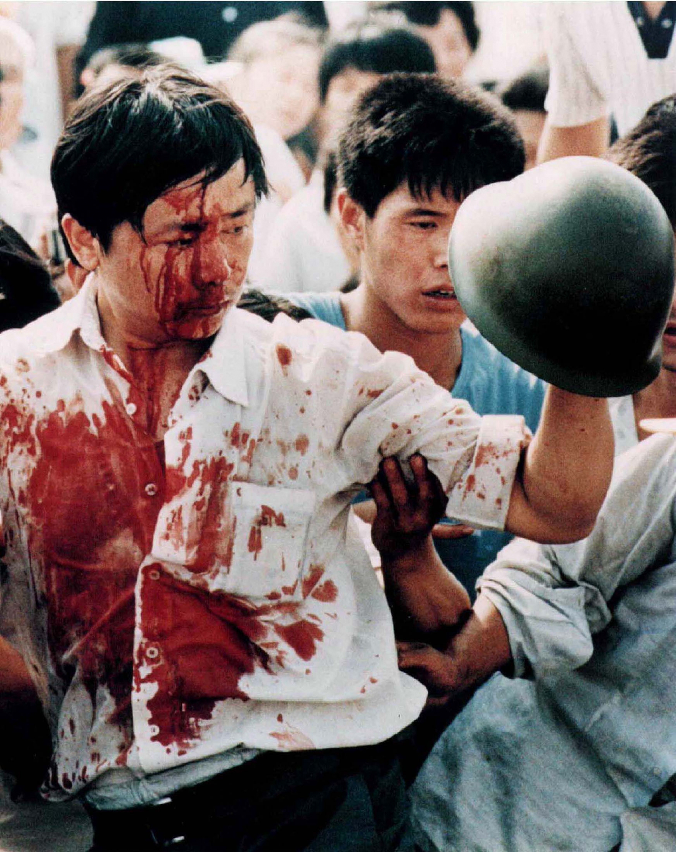 A protester is covered in blood as the Chinese military clears Tiananmen Square on June 4, 1989. A man is covered in blood while holding up a military helmet.