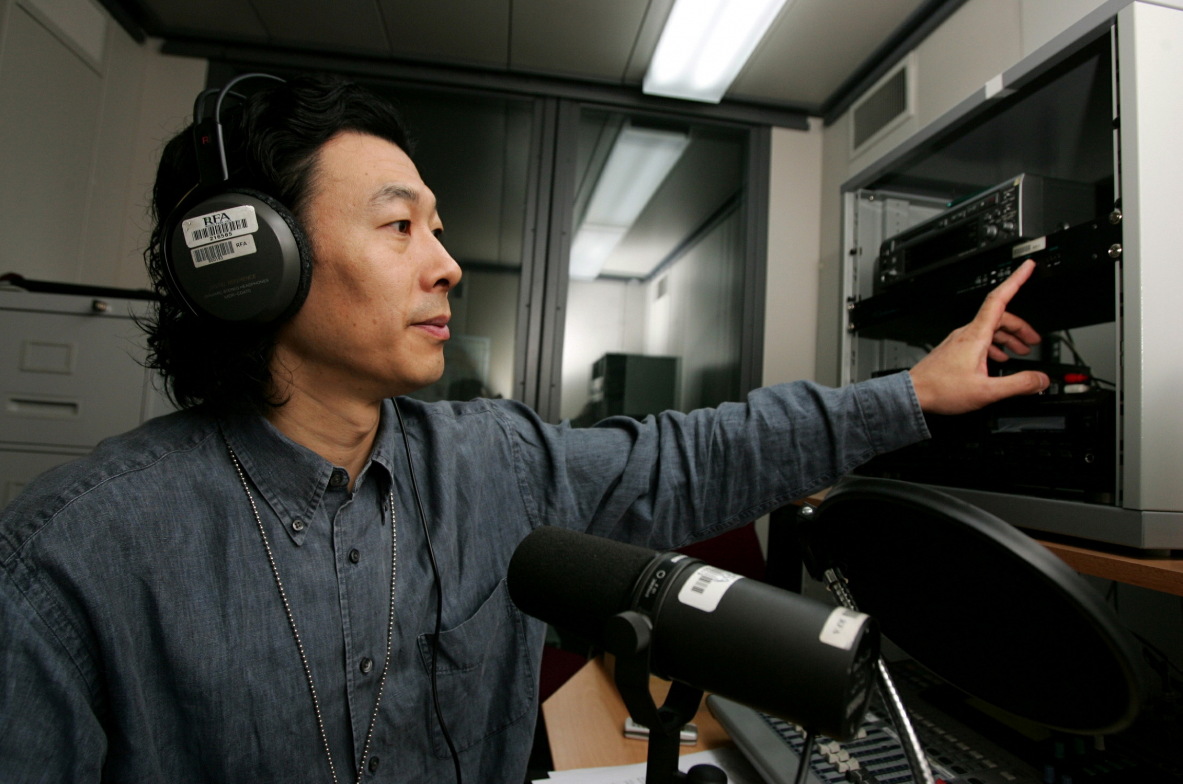 hinese labour activist Han Dongfang speaks on a radio show at his studio in Hong Kong. A man with headphones on speaks into a microphone in a studio.