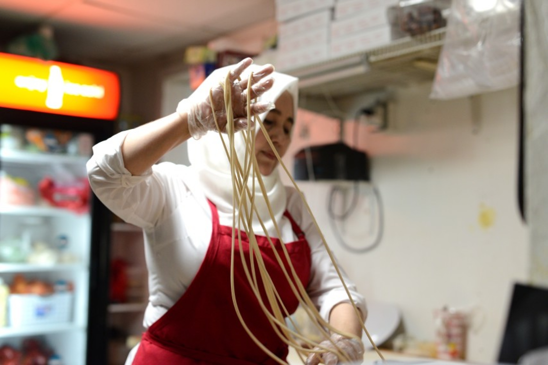 Silk Road offers diners hand-pulled noodles, a typical Uighur dish. A woman in a kitchen makes noodles.