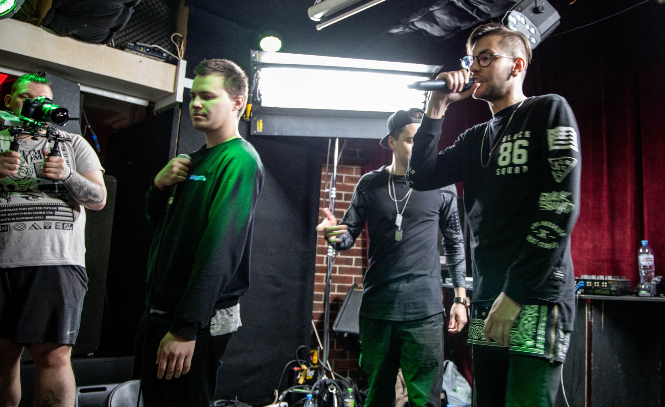 Rappers perform at the Alibi Club in Moscow Russia. When they perform covers, the crowd raps along with them, hands in the air. A man raps on a stage.