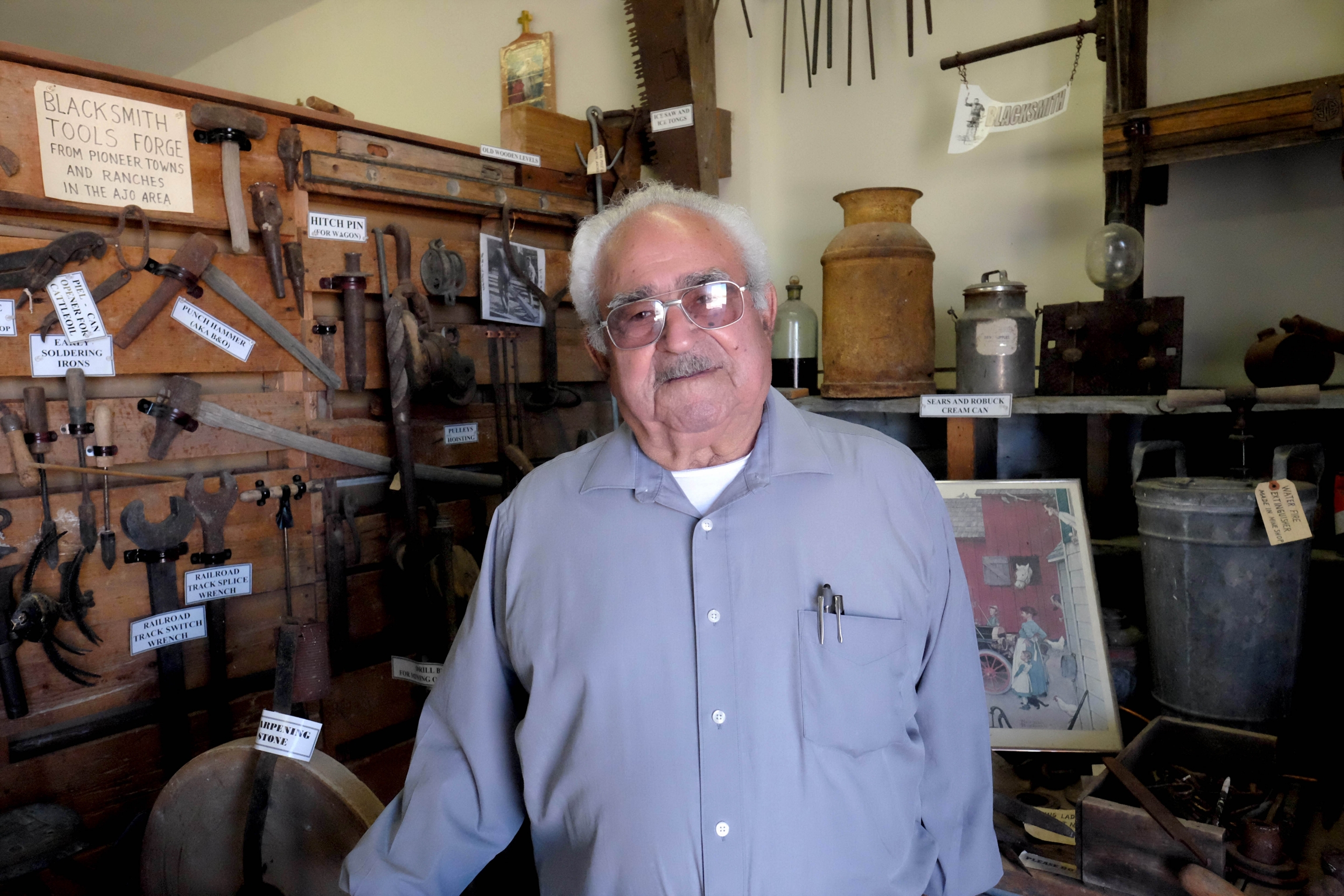 José Castillo, a longtime resident of Ajo, stands in front of a wall of photos and news clippings at the Ajo Historical Society Museum, where he is a volunteer. A man poses for a photograph