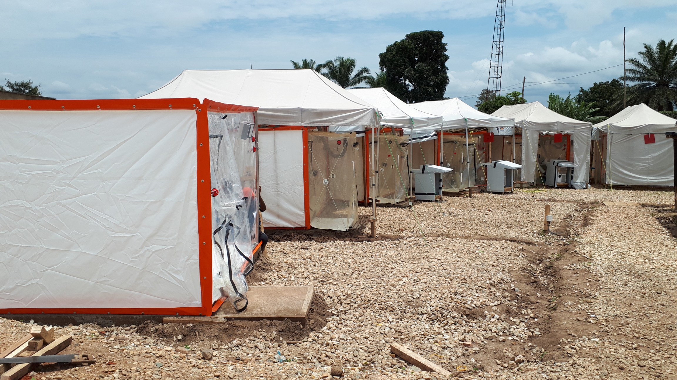 A row of transparent tents are set up on a gravel clearing