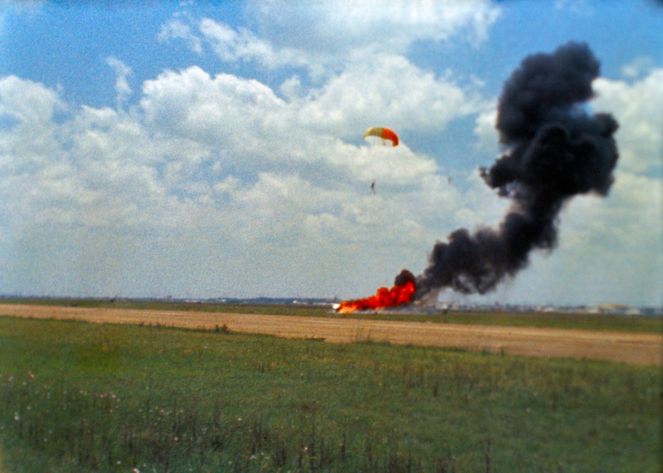 Neil Armstrong ejects from the Lunar Landing Research Vehicle which crashed during a landing simulation. An airfield is shown with Neil Armstrong and his parachute landing.