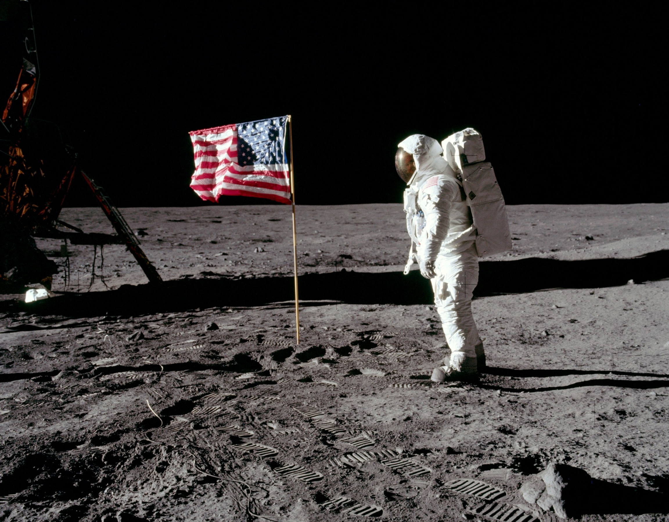 Astronaut Buzz Aldrin poses for a photograph beside the United States flag on the moon. Buzz Aldrin stands in his full astronaut suit facing the United States flag.