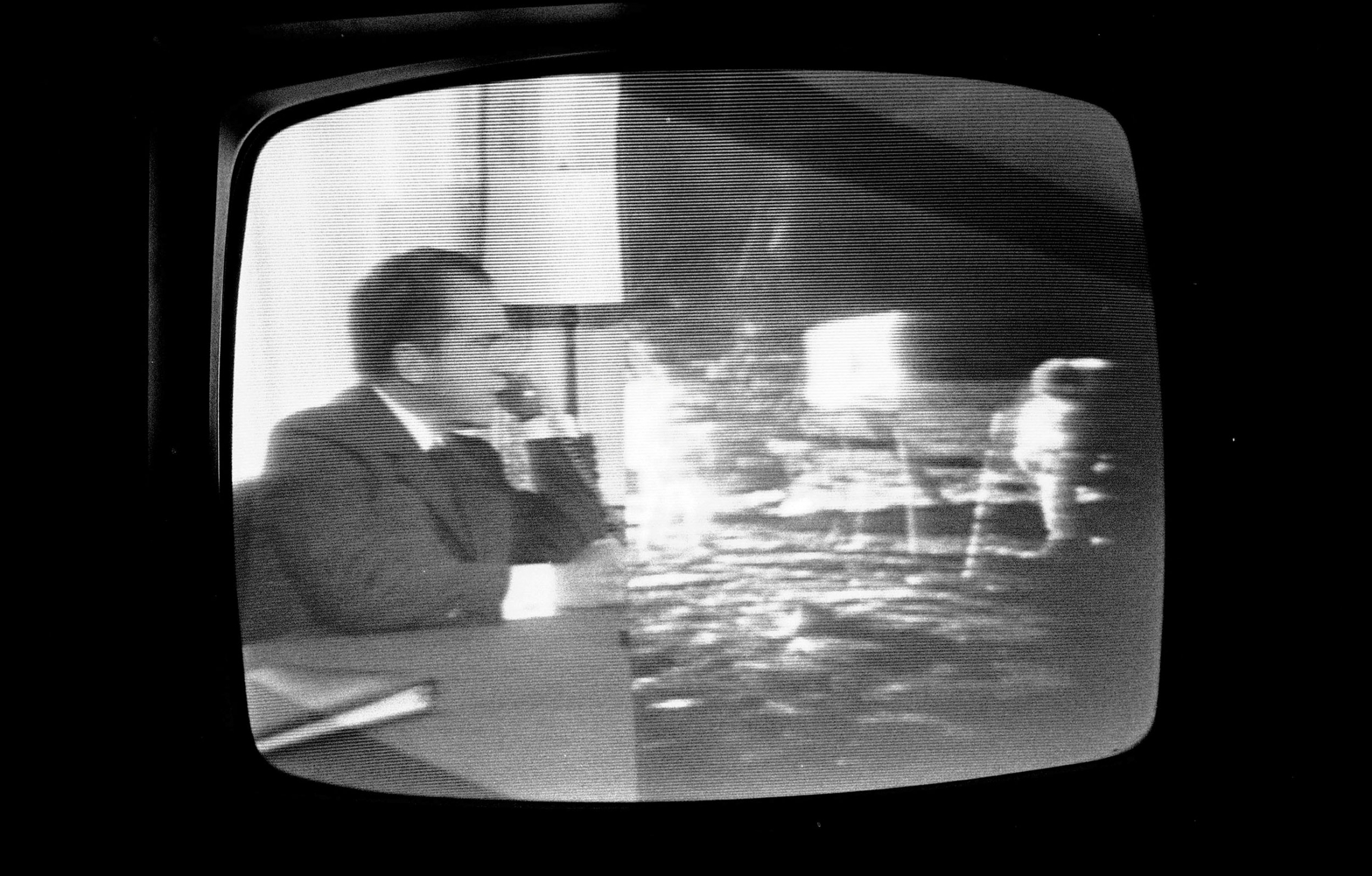 A television split-screen shot shows President Richard Nixon in the Oval Office speaking to the Apollo 11 astronauts on the moon as Buzz Aldrin and Neil Armstrong walk on the lunar surface, July 20, 1969. In a photograph of a television, President Richard Nixon is shown on the left and Apollo 11 crew is shown on the right all in black and white.