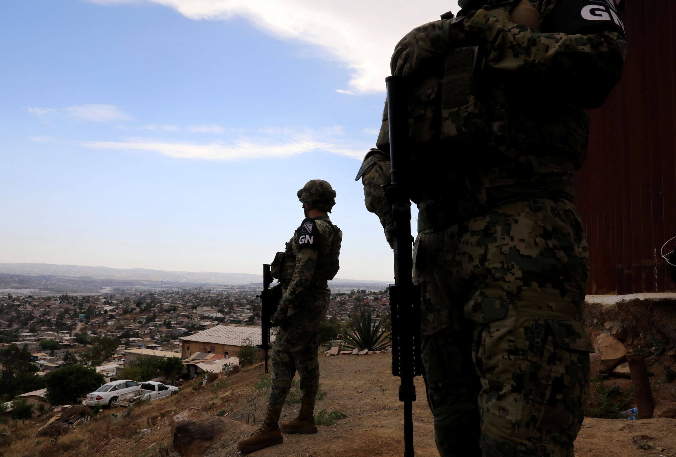 Members of the National Guard patrol next to the border fence between Mexico and US. Two security authorities are shown wearing military fatigues and carrying riffles.