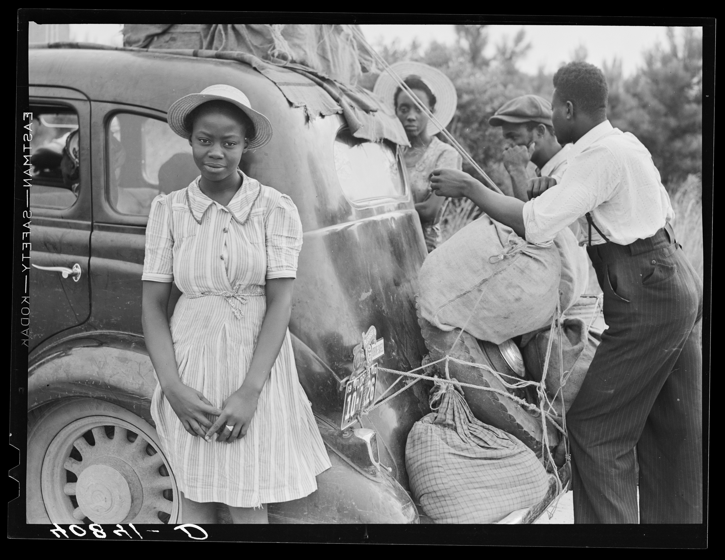 A 1940 photo of Florida migrants on their way to New Jersey to pick potatoes. A family is seen tying sacks of potatoes to a car.