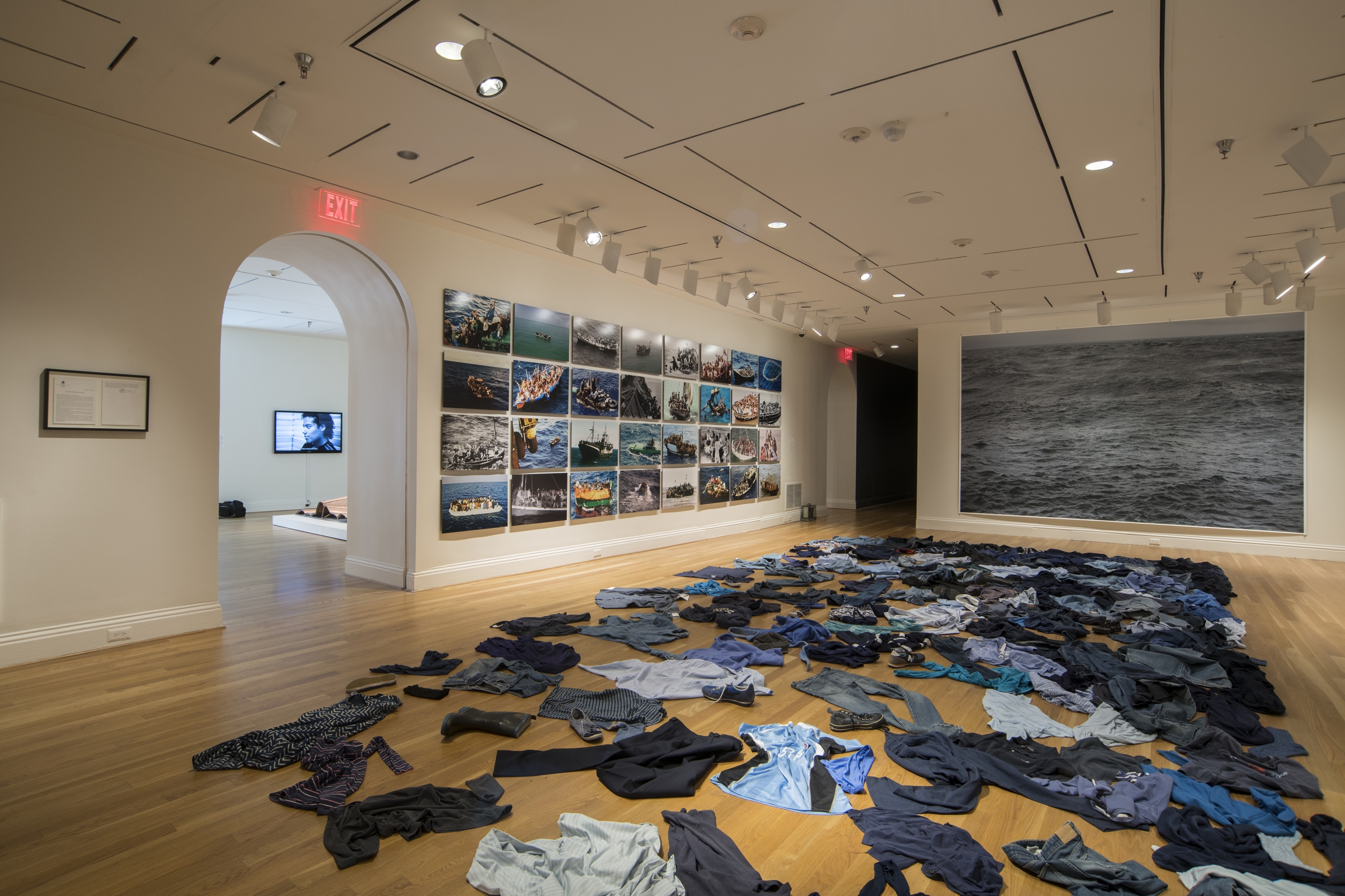 For “La Mer Morte (The Dead Sea),” French-Algerian artist Kader Attia covered the floor in blue clothing, as if the wearers had suddenly disappeared into the sea. Dark colored clothes are strewn on the floor in an art exhibition.