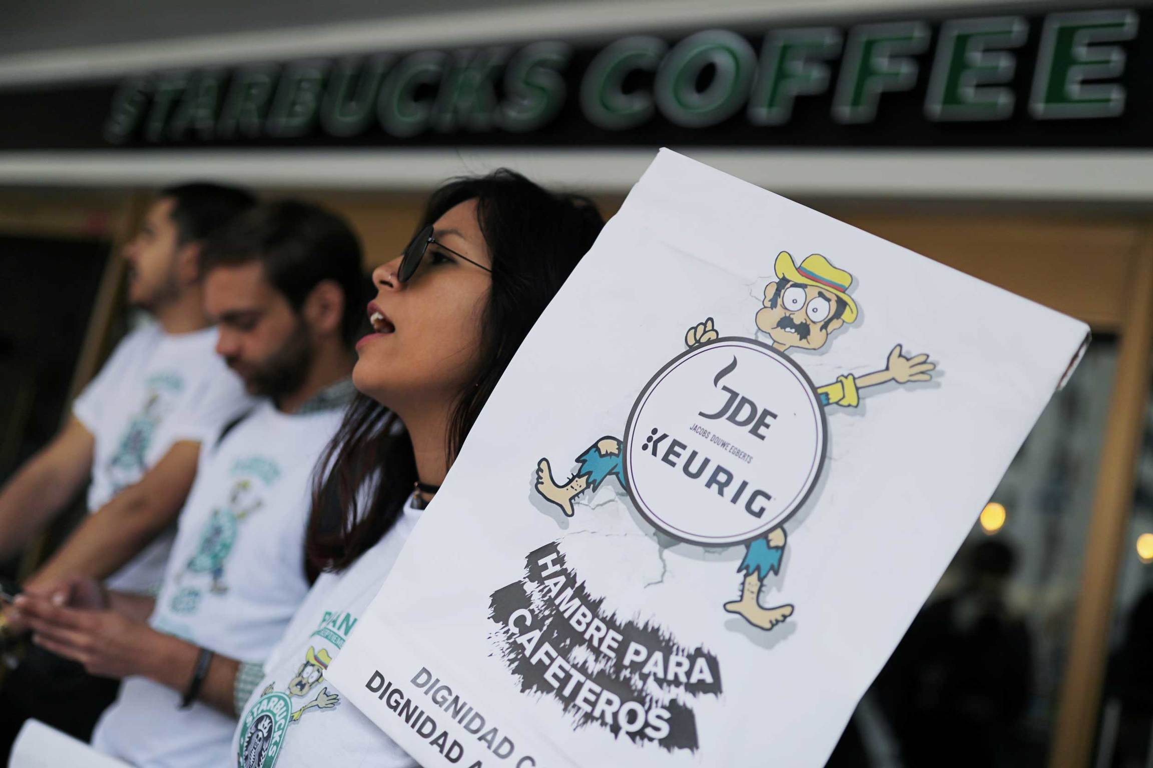 A protester holds a sign in Spanish that reads "Hunger for coffee growers." A protester holds a sign in Spanish that reads "Hunger for coffee growers."