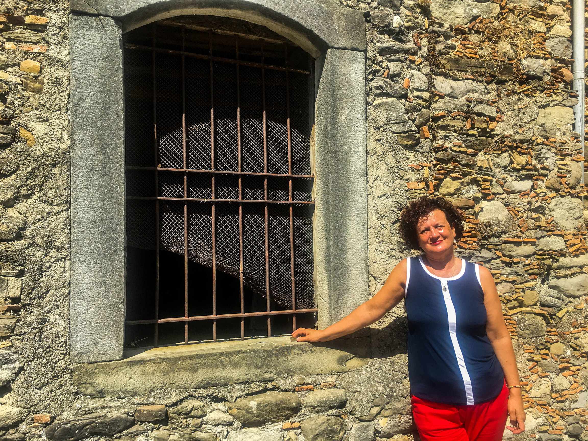 The first house to go on the market is owned by Maria Concetta Abramo, who is pictured. A woman is shown leaning on a stone building and wearing a blue shirt and red pants.