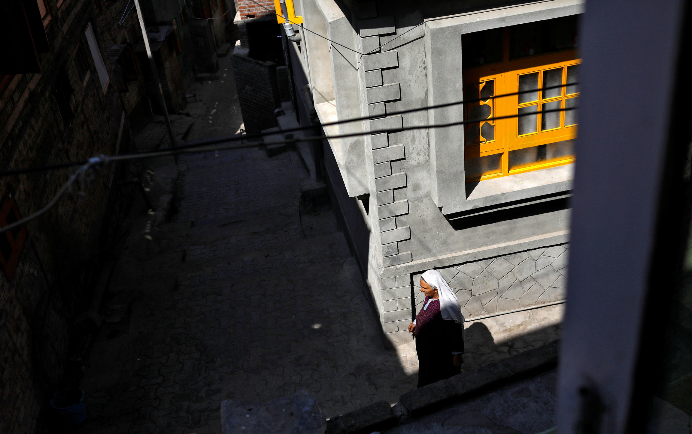 A Kashmiri woman walks through an empty street in Anchar. A woman is shown wearing a purple gown and white headscarf passing through the street.