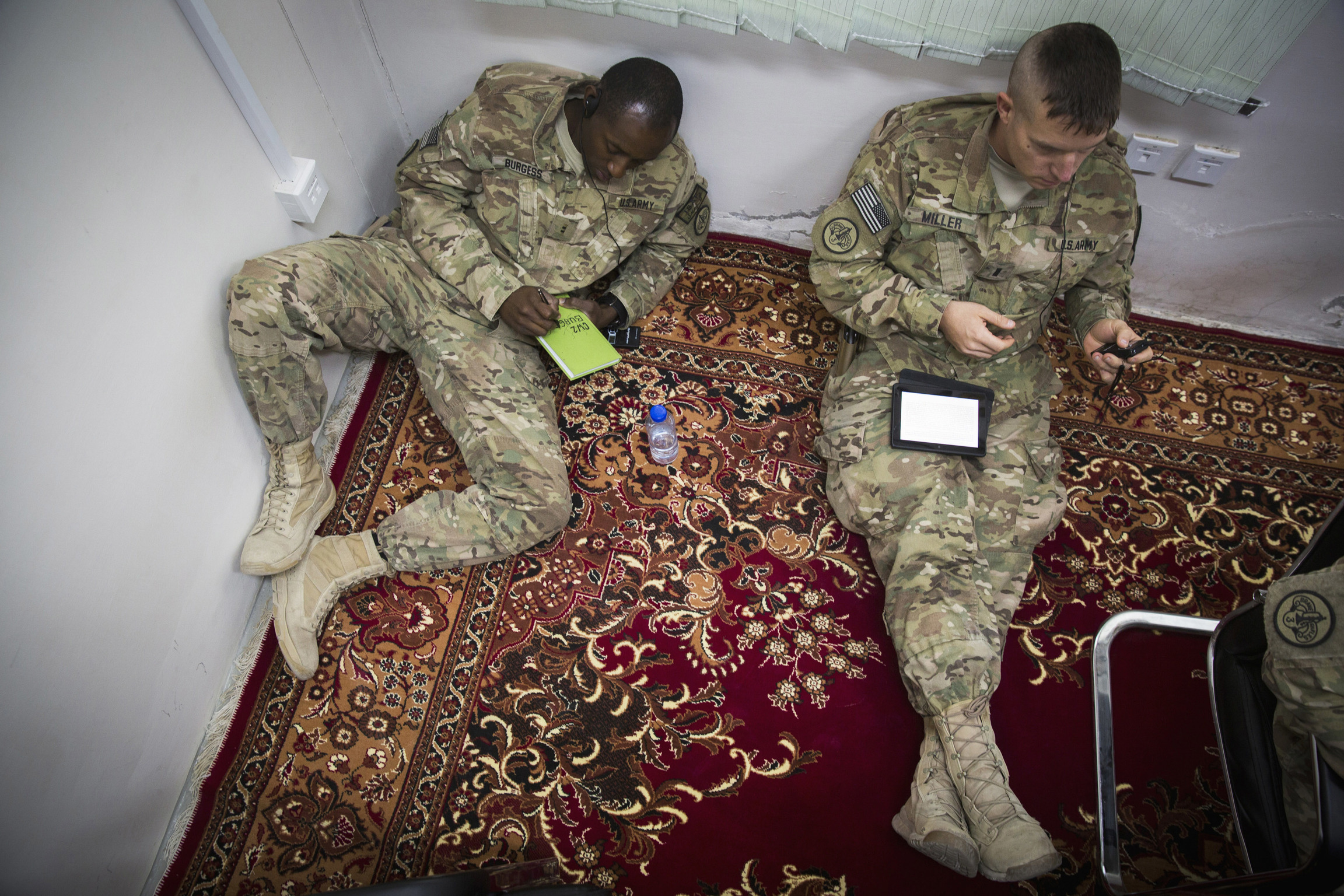 Two US soldiers listen to a translator and take notes on red carpet