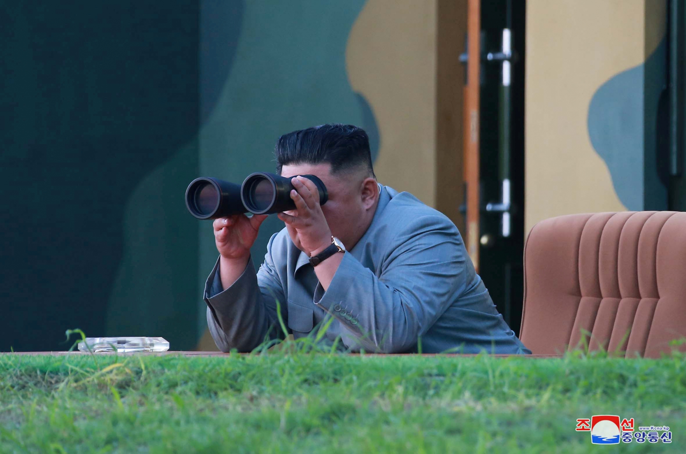 Kim Jong-un looks through binoculars and leans over a ledge