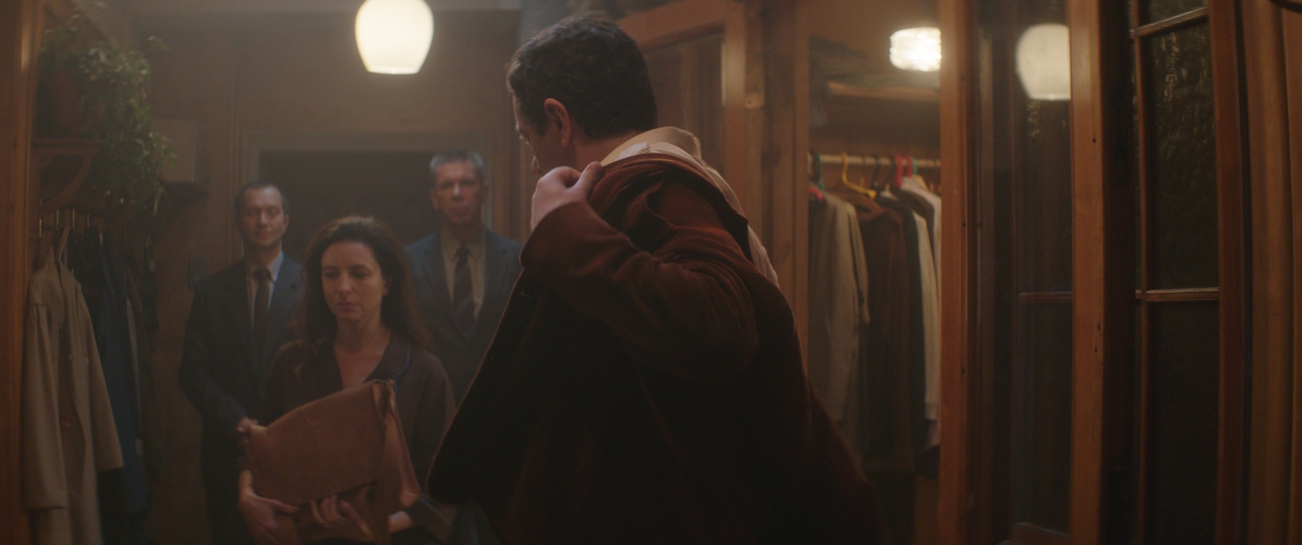 KGB visit A sepia-toned film still, two men in suits stand in the background, a woman in the midground is upset, a man in the foreground puts on his coat.