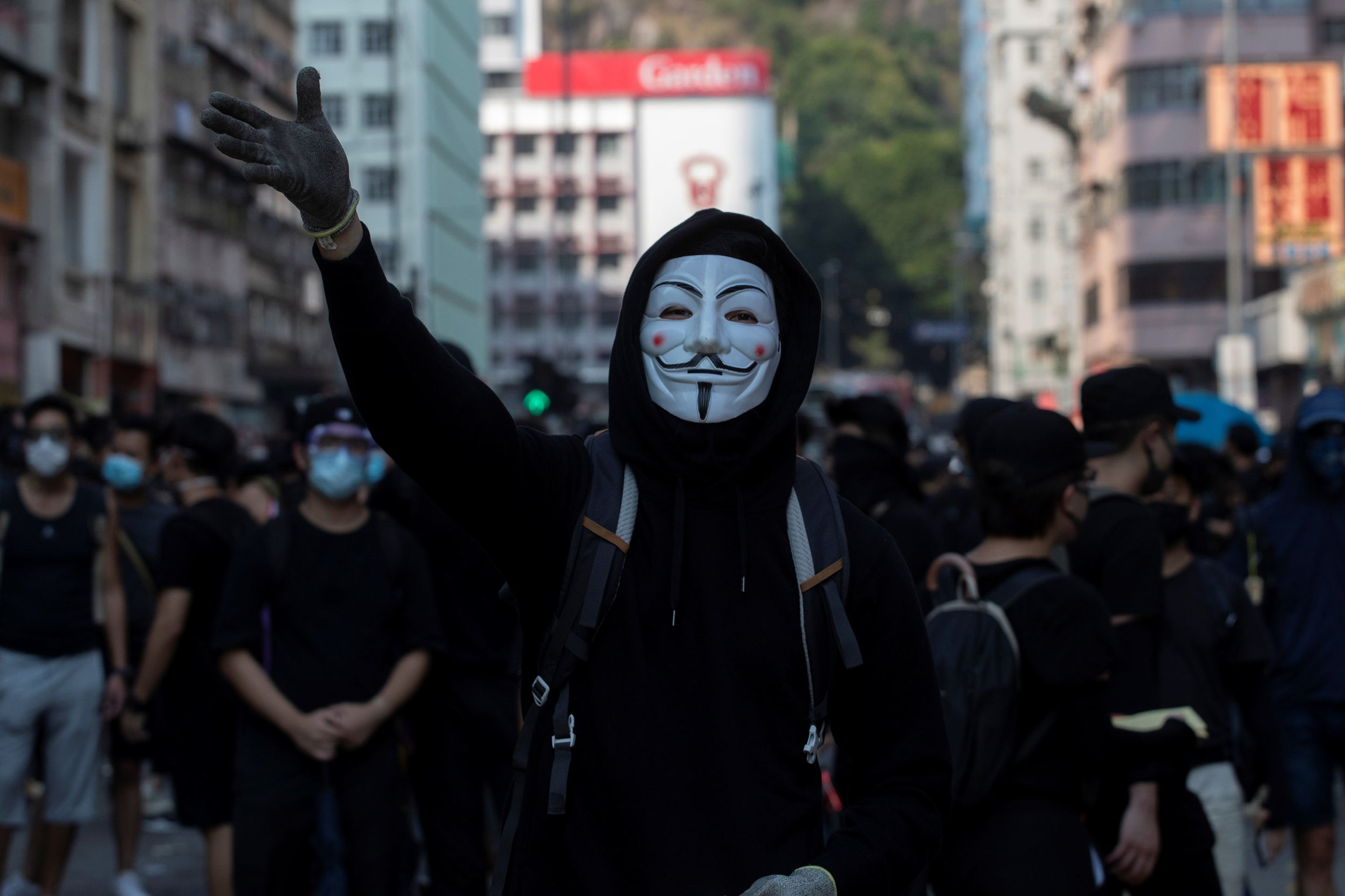 An anti-government protester wearing a Guy Fawkes mask attends a protest on China's National Day in Hong Kong, Oct. 1, 2019. A person is shown center frame wearing a Guy Fawkes maks with their right raised hand in the air.