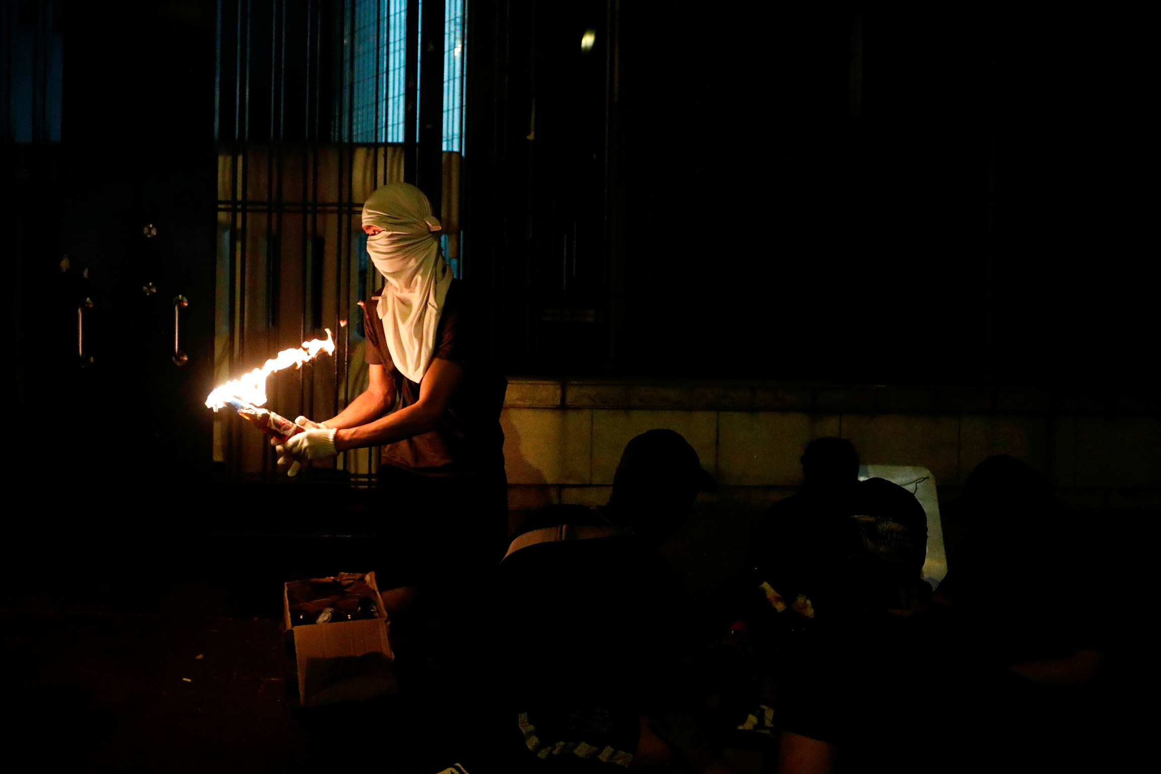 An anti-government protester holds a Molotov cocktail in front of New Territories South Regional Headquarters in Hong Kong, Oct. 2, 2019. An anti-government protester is shown holding a Molotov cocktail set ablaze and wearing white mask covering his face and head.