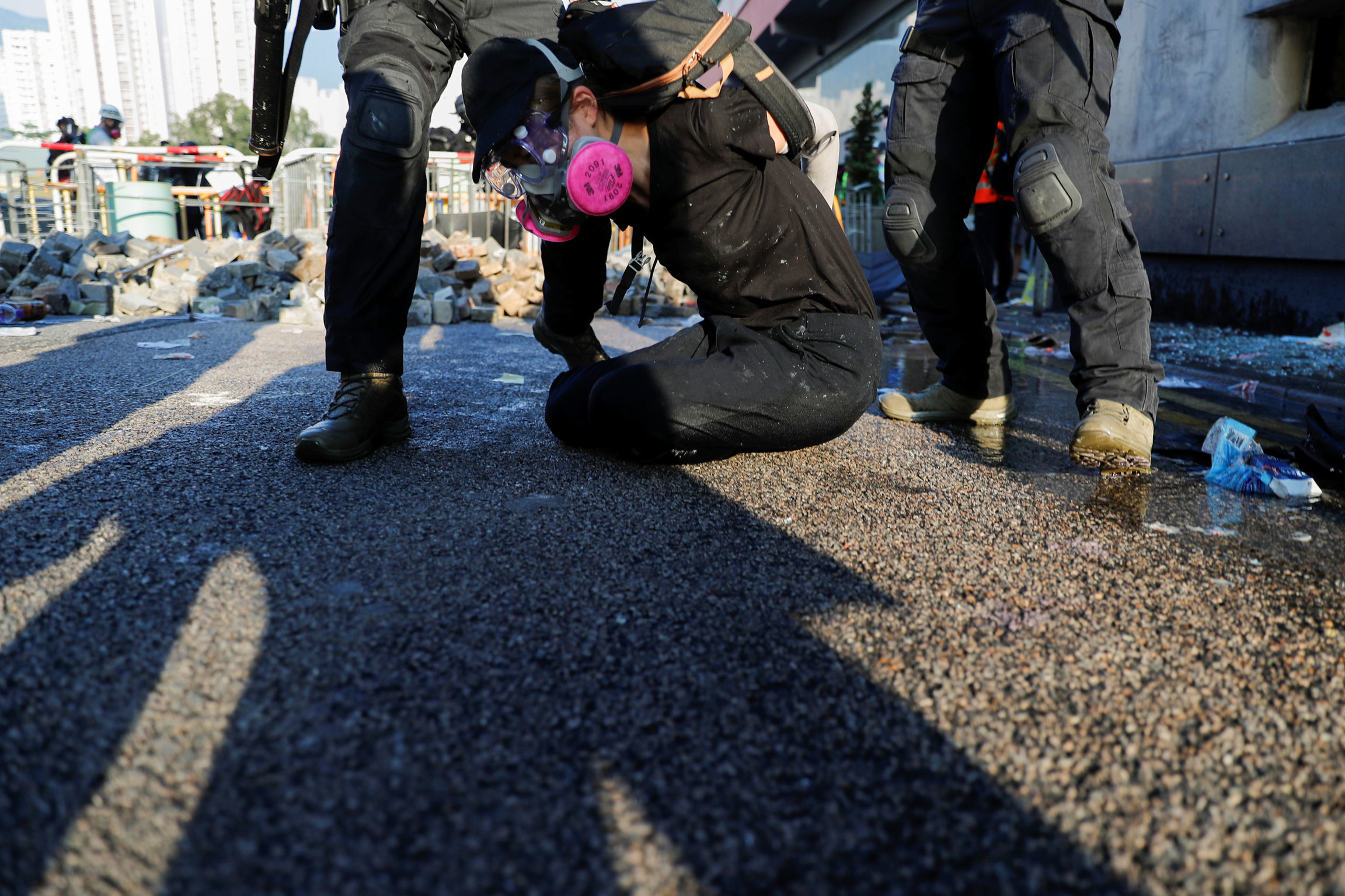 An anti-government protester is detained by riot police during a demonstration on Oct. 1, 2019. A person is shown on the grown with their hands held behind their back and wearing a pink gas mask.
